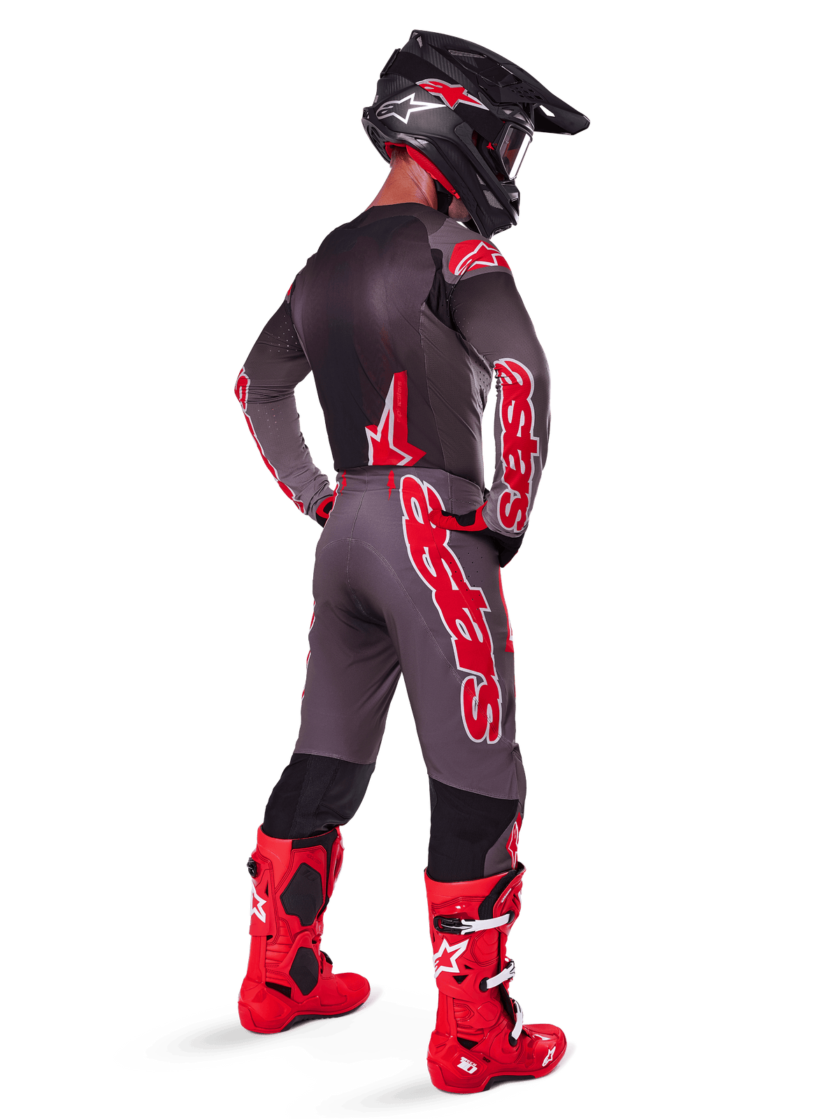 Motocross-Fahrer in Alpinestars 2025 Supertech Lipan Hose, Smoke Bright Red, graue Hose mit großen roten Logos und schwarzen Innenbein-Einsätzen, kombiniert mit passendem grauen Trikot, schwarzem Helm und leuchtend roten Stiefeln, komplettes Offroad-Rennoutfit in der Rückansicht.