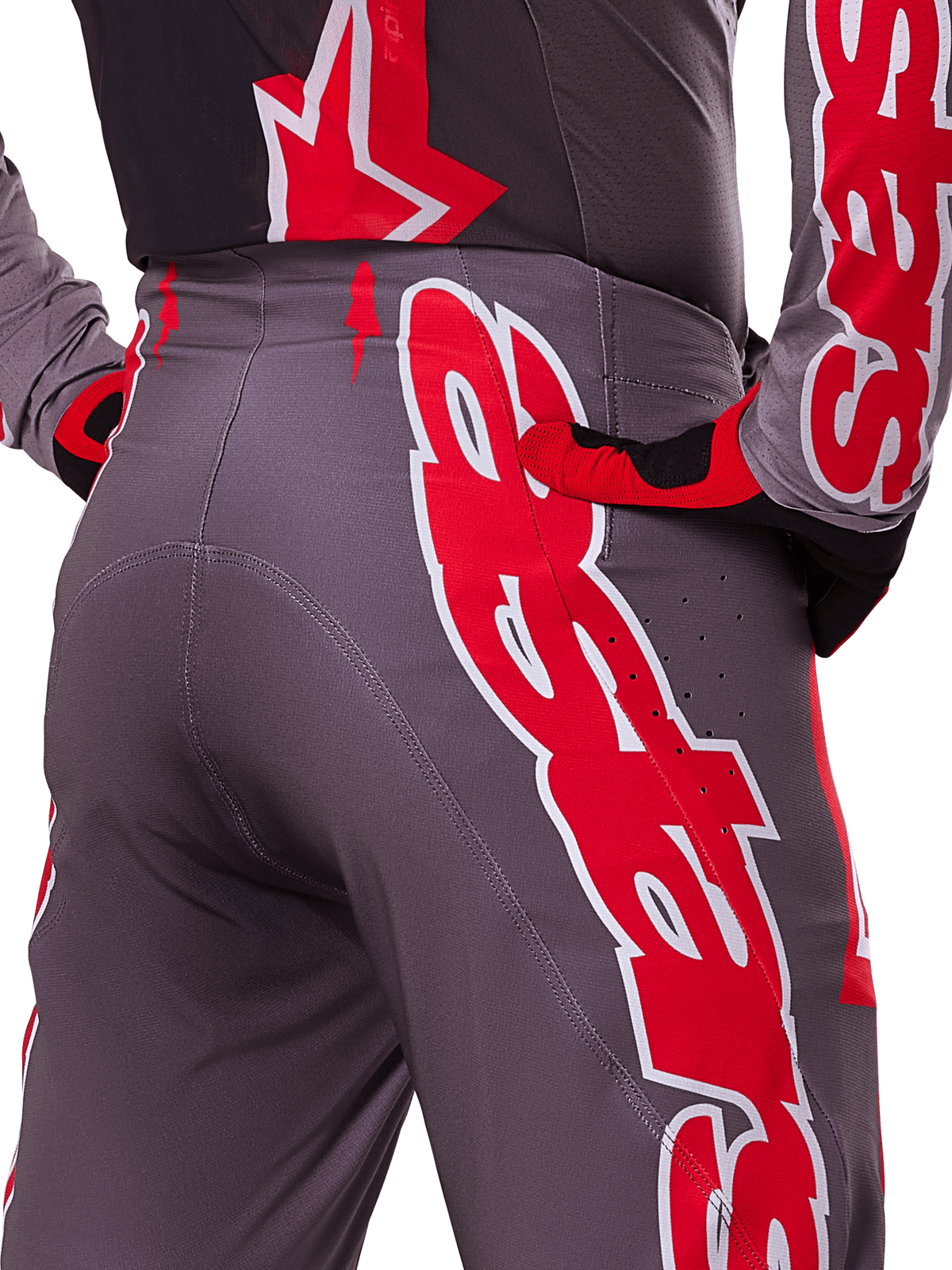 Alpinestars 2025 Supertech Lipan Hose, Motocross-Hose, Smoke Bright Red, Nahaufnahme der Rückansicht mit dunkelgrauem Gewebe und markanten roten Grafiken, getragen mit passenden roten und schwarzen Handschuhen und Trikot, mit Belüftungsperforationen und ergonomischen Nähten für Offroad-Performance