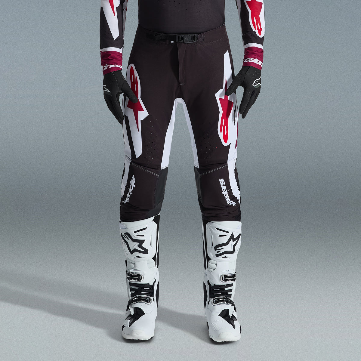 Alpinestars 2026 Supertech AFD Vista Gear Set, Motocross rider wearing black pants with large white and red logos, matching performance jersey with burgundy cuffs, black gloves, and white professional racing boots, high-performance off-road racing outfit