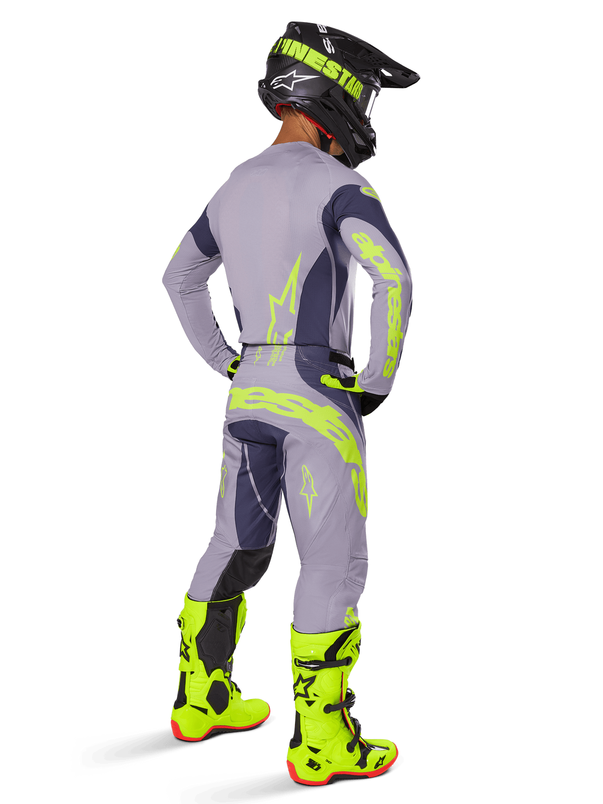 Motocross-Fahrer von hinten gesehen in kompletter Rennausrüstung, Alpinestars 2025 Techstar Dreem Hose in Grau und Dunkelgrau mit auffälligen neongelben Akzenten, passendes graues Trikot mit Neon-Grafiken, leuchtend neongelbe Stiefel und schwarzer Helm, professionell abgestimmtes Motocross-Outfit