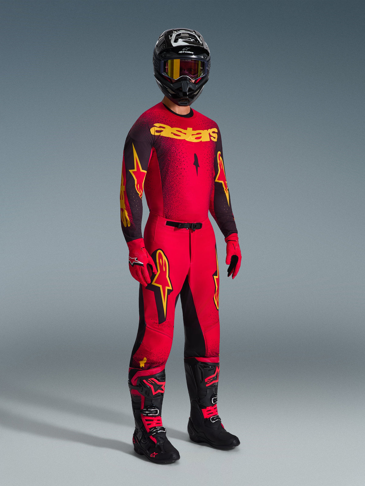 Alpinestars 2026 Supertech Scenz Hose, Motocross-Hose, Rot, Schwarz und Gelb, getragen von einem Fahrer in einer kompletten Rennausrüstung mit passendem Trikot und Stiefeln, mit markanten gelben und schwarzen Stern-Logos und einer athletischen Passform.