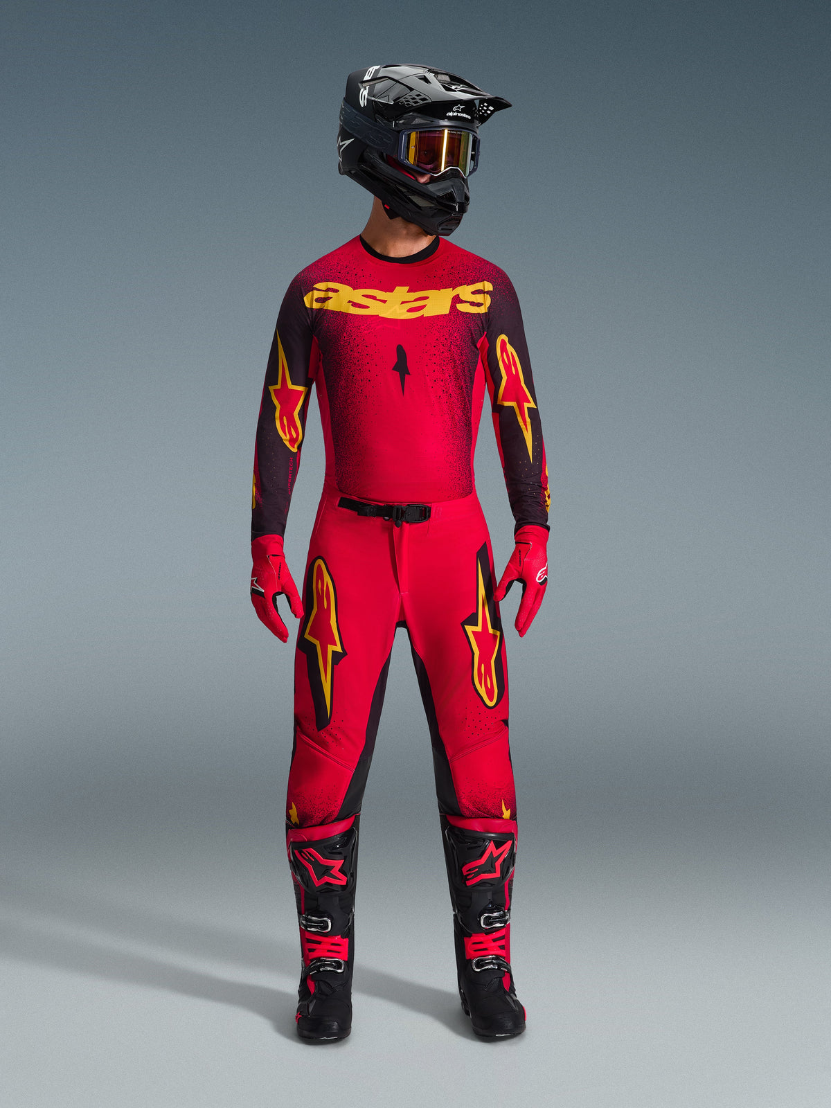 Alpinestars 2026 Supertech Scenz Hose, Motocross-Hose, Rot, Schwarz und Gelb, getragen von einem Fahrer in kompletter Rennausrüstung, passendes rot-schwarzes Trikot mit gelben Logos, schwarzer Helm, rote Handschuhe und schwarze Stiefel, sportliches Pro-Fit-Design für Offroad-Wettbewerbe