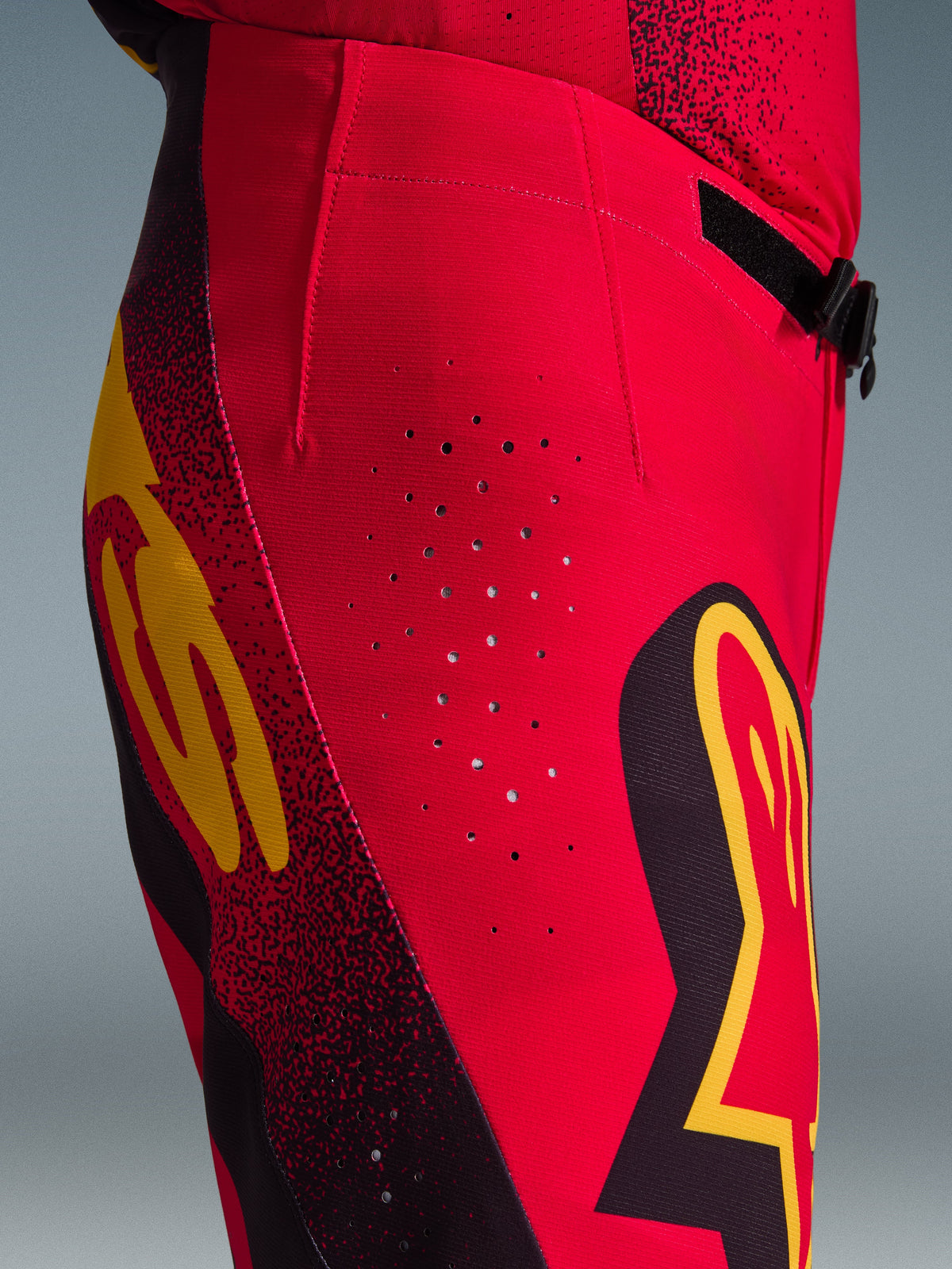 Alpinestars 2026 Supertech Scenz Hose, Motocross-Hose, Rot, Schwarz und Gelb, Nahaufnahme der Seitenansicht mit lasergeschnittenen Belüftungsperforationen, markanten Grafik-Logos und leistungsstarkem Stretch-Ripstop-Gewebe für Motocross-Rennsport.