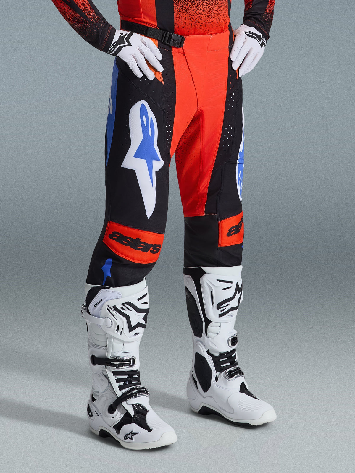 Alpinestars 2026 Techstar Knif Pants, Motocross Pants, Orange Black and UCLA Blue, worn with white gloves and white and black motocross boots, featuring bold logos on the thighs and orange knee panels with astars branding.