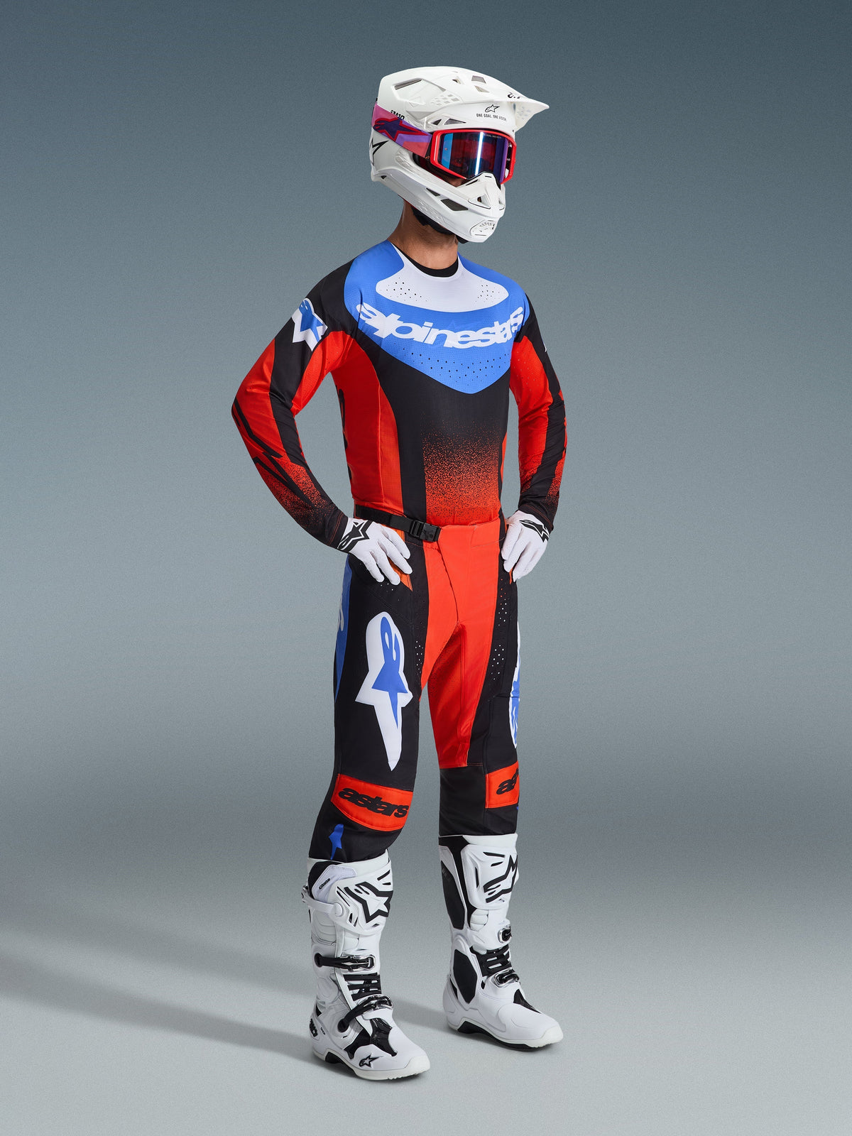 Motocross rider wearing the 2026 Techstar Knif Pants in Orange, Black, and UCLA Blue, paired with a coordinating racing jersey, white helmet with red and blue goggles, and white off-road boots, complete professional gear set for motocross.