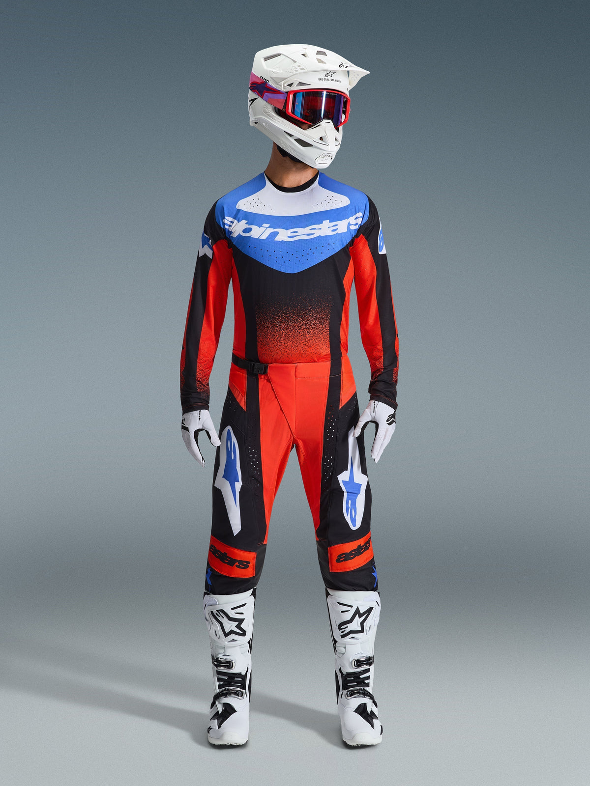 Motocross rider wearing complete racing gear, Orange and black jersey with blue accents, Orange black and UCLA blue Techstar Knif pants, white helmet with red goggles, white and black boots, white and black gloves, coordinated outfit for off-road racing