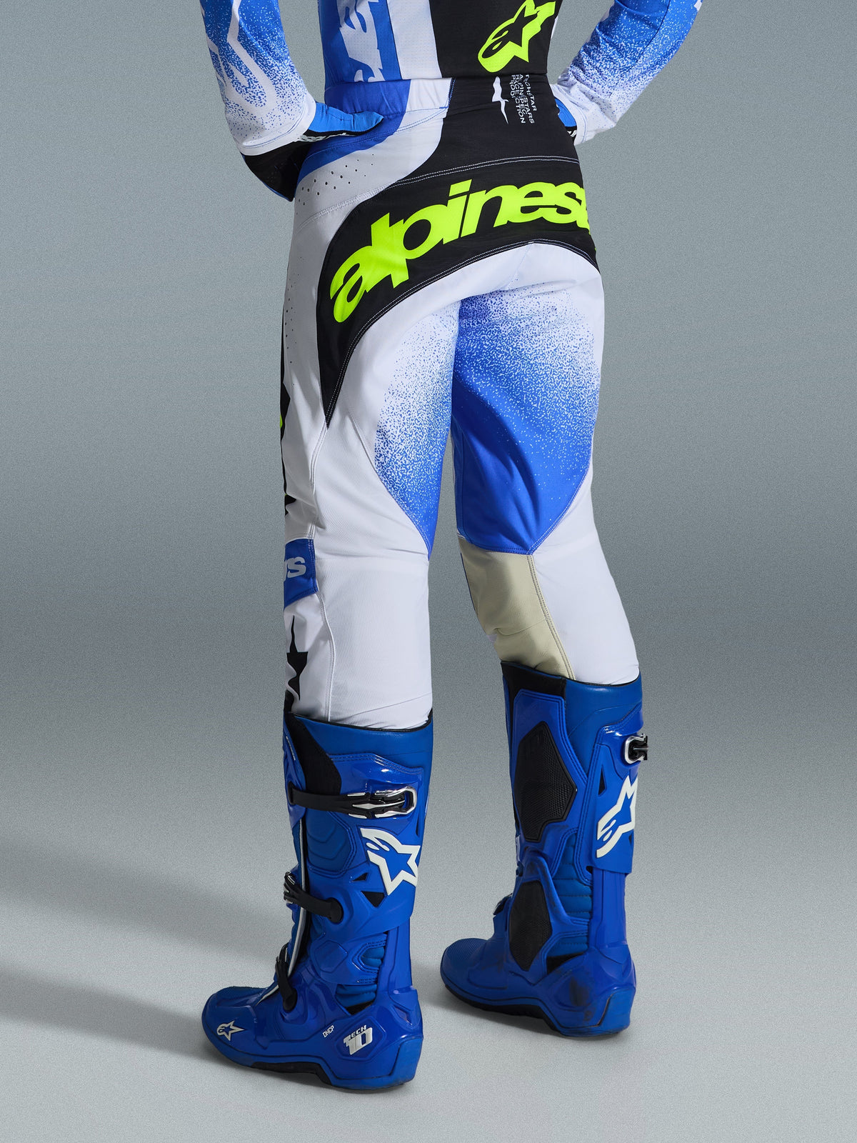Alpinestars 2026 Techstar Knif Pants, Motocross Pants, Ucla Blue Black and Yellow Fluo, rear view featuring white panels with blue gradient spray pattern, bold yellow-fluo branding on the black seat, worn with matching blue Tech 10 boots and jersey for off-road racing.