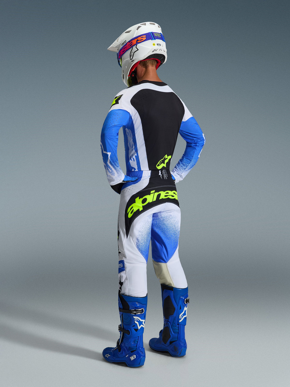 Motocross rider shown from the back wearing the 2026 Techstar Knif Pants in Ucla Blue Black and Yellow Fluo, featuring bright yellow branding on the seat, coordinated jersey with blue sleeves, white helmet, and blue off-road boots.