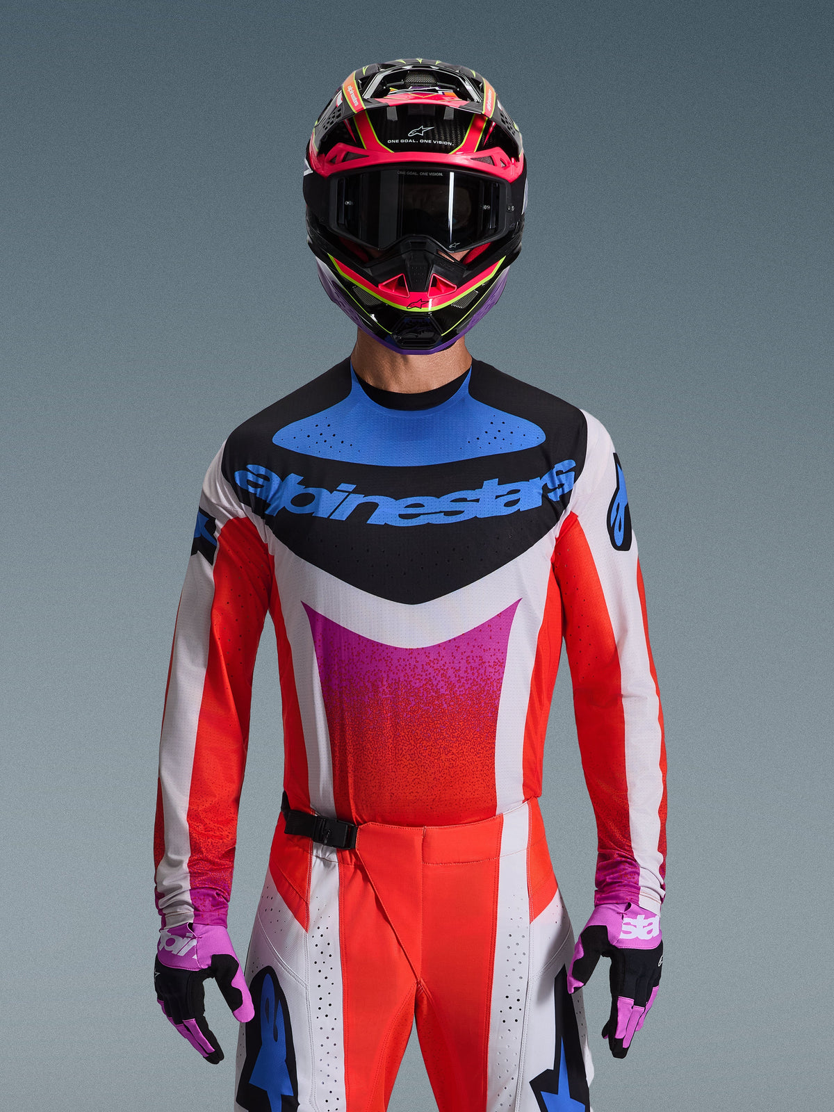 Motocross-Fahrer im 2026 Techstar Knif Gear Set, weißes Trikot mit roten Ärmeln und blau-pinker Brustgrafik, passend rot-weiße Hose, leuchtend pink-gelber Helm mit dunkler Schutzbrille und lila-schwarze Handschuhe, professionelle Ausrüstung für den Offroad-Rennsport.