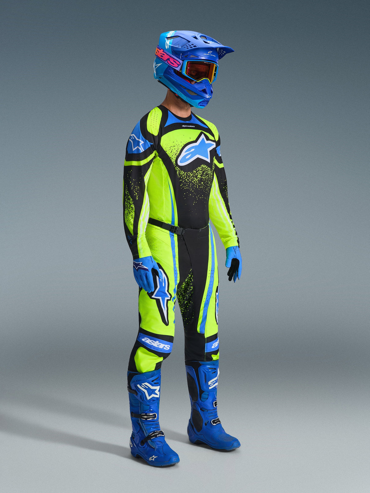 Motocross rider wearing complete racing gear, Yellow fluo jersey with dark navy and blue accents, Alpinestars 2026 Techstar Nomur Pants in matching colors, blue helmet with goggles, blue and black boots, blue gloves, coordinated outfit for off-road racing