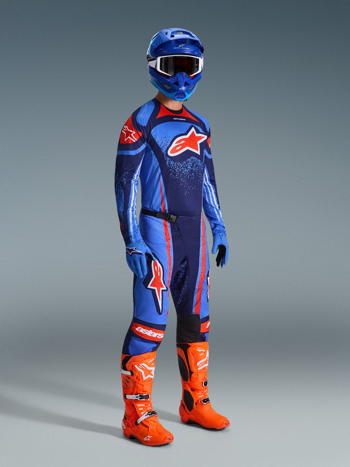 Alpinestars 2026 Techstar Nomur Hose, Motocross-Hose, Dunkelblau, Orange und UCLA-Blau, getragen von einem Fahrer in kompletter Rennausrüstung mit passendem Trikot, blauem Helm und leuchtend orangen Stiefeln, leistungsorientiert für Offroad-Rennsport entwickelt