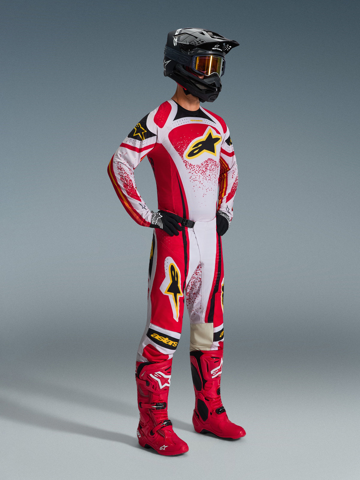 Motocross-Fahrer im Alpinestars 2026 Techstar Nomur Gear Set, Rot und Weiß mit schwarzen Akzenten und gelben Logos, getragen mit passenden roten Stiefeln und einem schwarzen Helm, professionelle Rennausrüstung für Offroad-Wettbewerbe