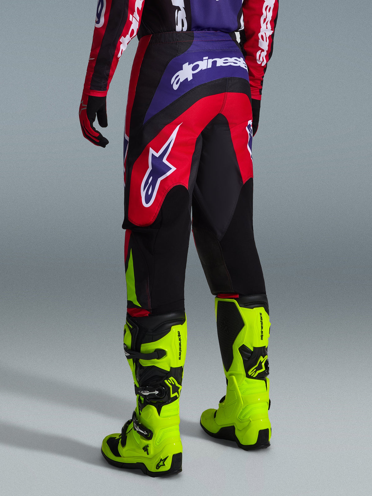 Alpinestars 2026 Fluid Grid Pants, Motocross Pants, Red Black and Purple, rear view showing large white logo, worn with neon yellow racing boots and matching jersey, durable sport-fit design for off-road performance