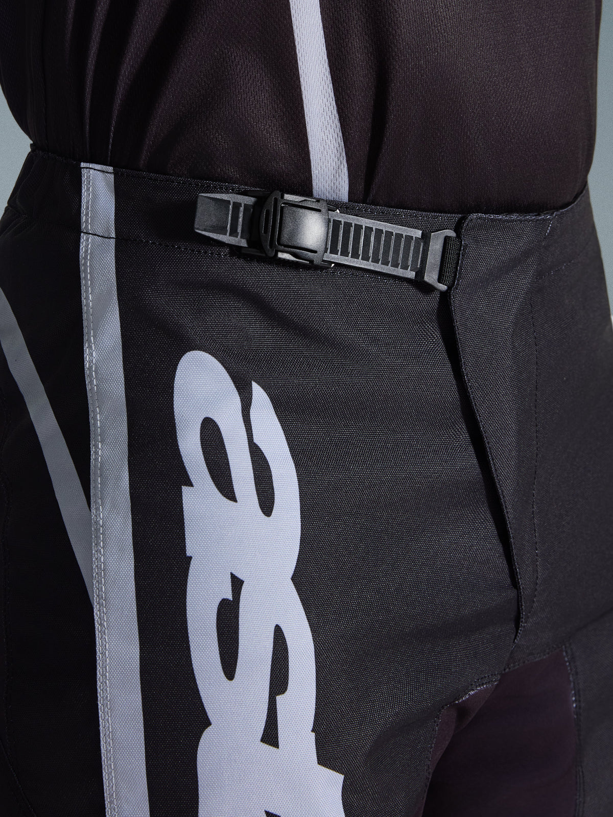 Alpinestars 2026 Fluid Apex Hose, Motocross-Hose, Schwarz und Grau, Nahaufnahme des integrierten Ratschenverschluss-Systems für eine sichere Passform, mit weißen Logo-Grafiken auf strapazierfähigem 600D-Polygewebe.
