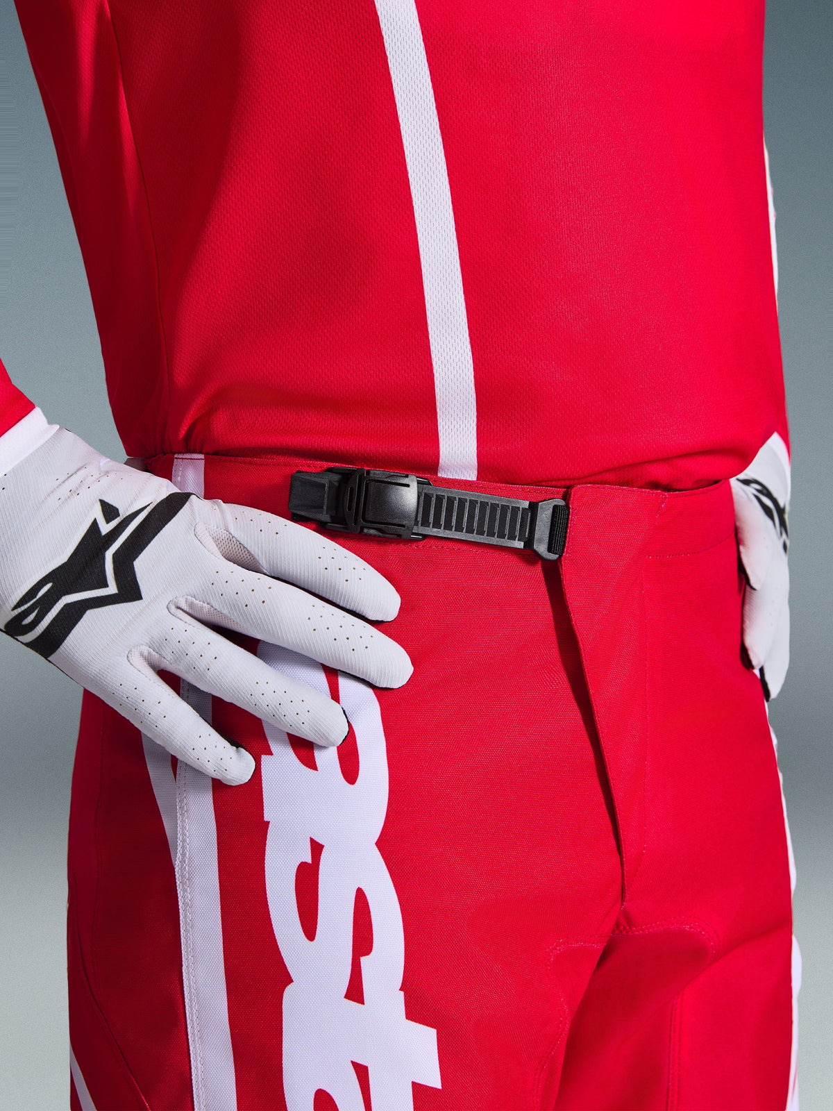 Alpinestars 2026 Fluid Apex Pants, Motocross Pants, Red and White, close-up of the black ratchet waist closure system, worn with white Alpinestars gloves and matching red jersey, durable performance gear for off-road riding.