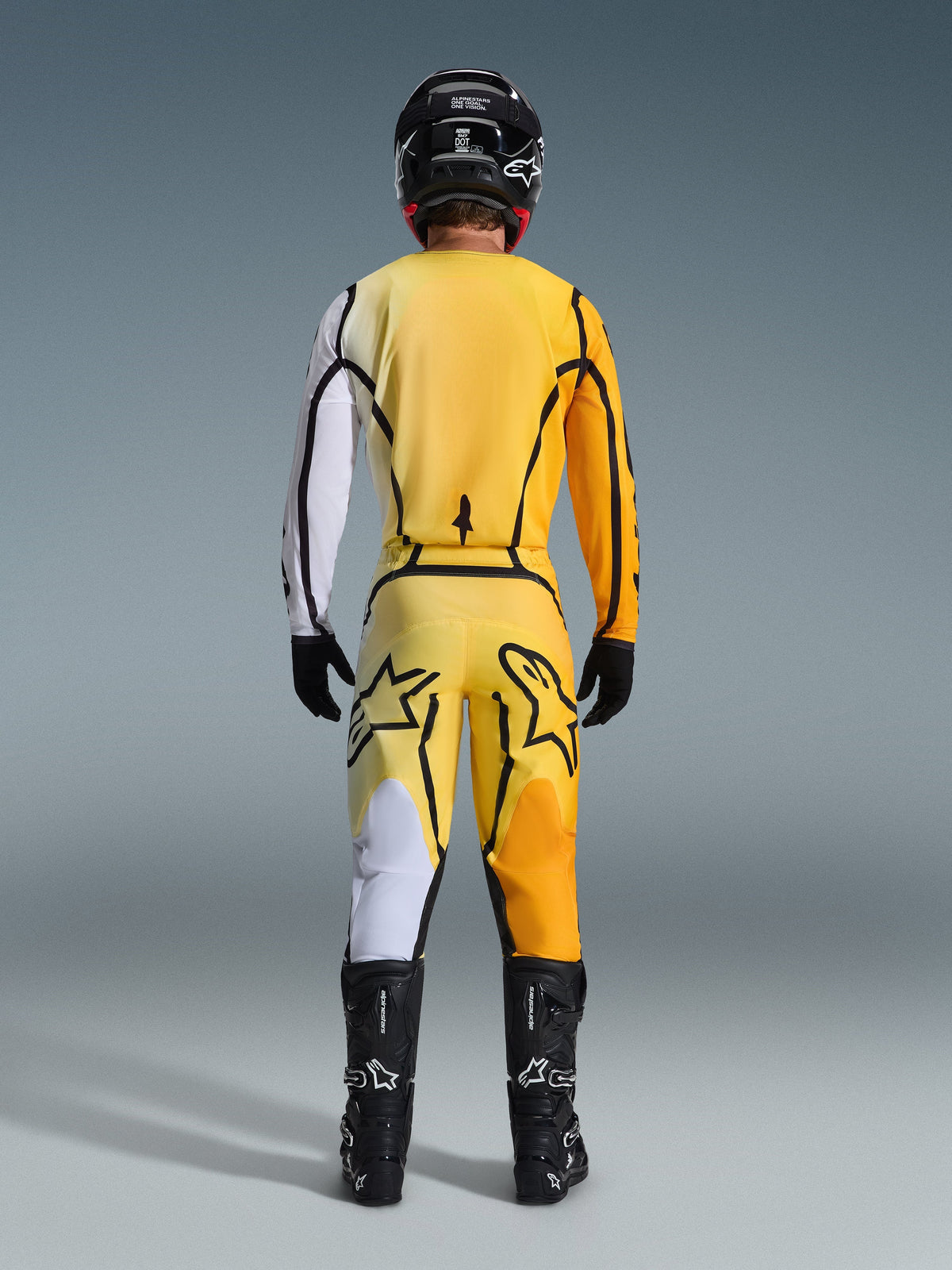 Alpinestars 2026 Fluid Apex Hose, Motocross-Hose, Gelb und Schwarz, Rückansicht eines Fahrers in kompletter Motocross-Ausrüstung, passendes Trikot mit weiß-orangen Farbverläufen, schwarzer Helm, schwarze Stiefel und schwarze Handschuhe, abgestimmtes Offroad-Outfit.