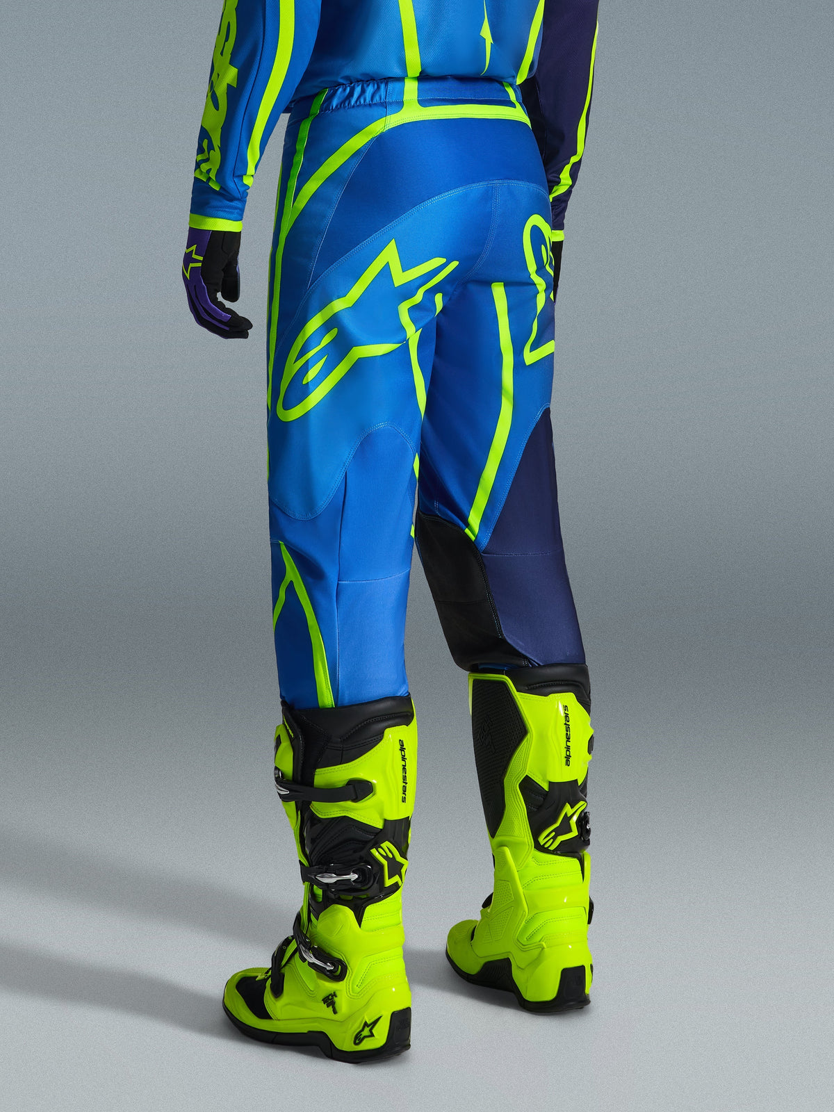 Alpinestars 2026 Fluid Apex Pants, Motocross Pants, Blue and Yellow Fluo, back view of rider wearing matching gear and fluorescent yellow boots, featuring bold Alpinestars logos and ergonomic design