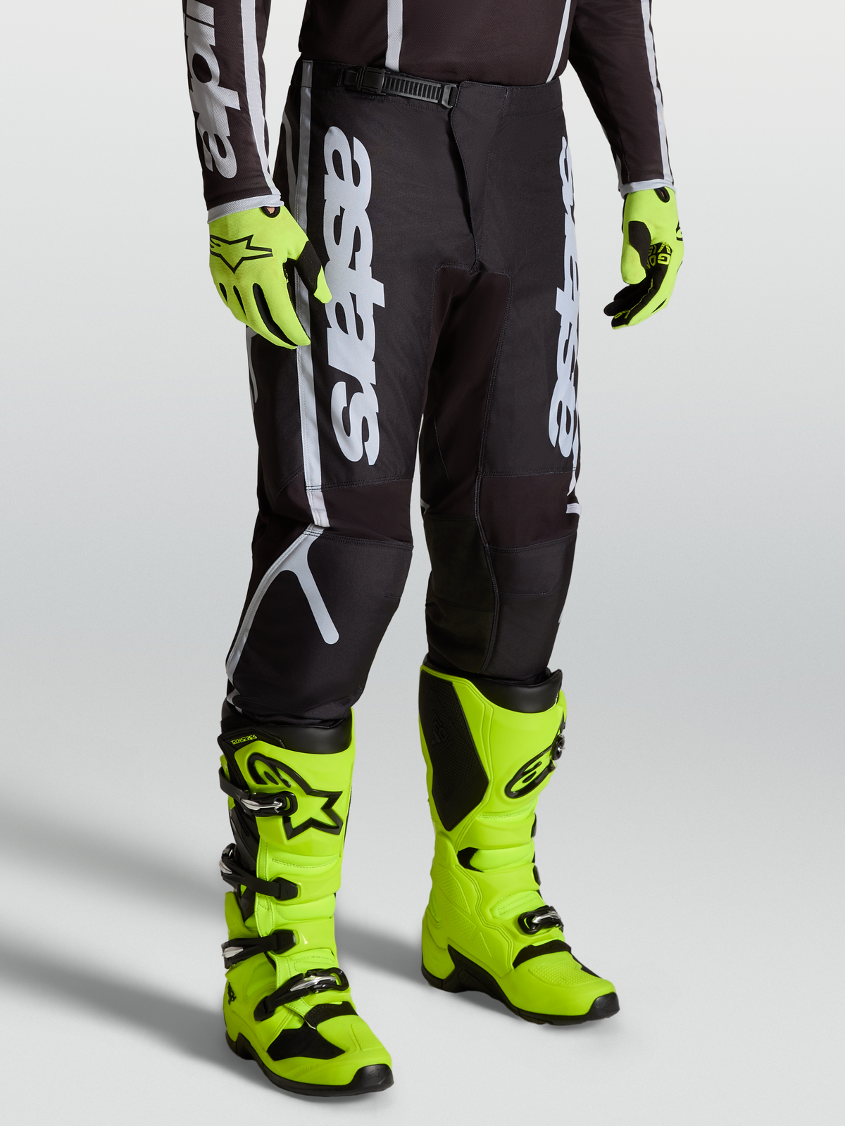 Alpinestars Fluid Apex V2 Pants, Men’s Motocross Gear in Black and Silver, featuring Alpinestars branding and durable 600D polyfabric. Shown on-model with bright yellow boots.