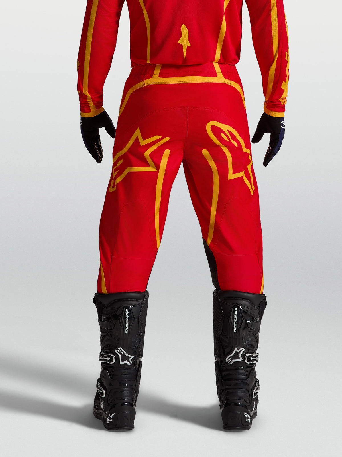 Alpinestars Fluid Apex V2 Hose, Motocrosshose für Herren in Feuerrot und Gold, Rückansicht mit schwarzen Motorradstiefeln.