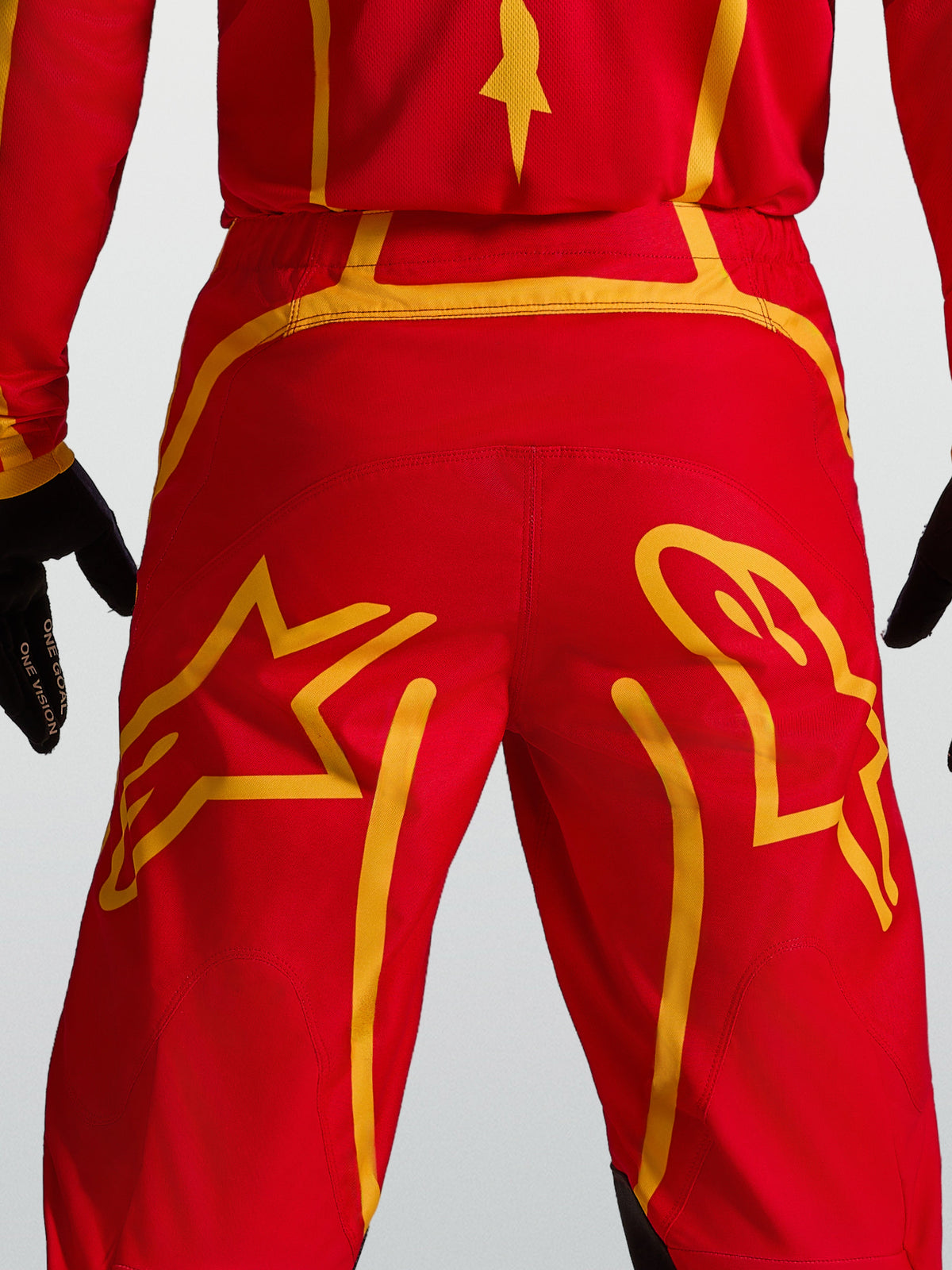 Alpinestars Fluid Apex V2 Hose, Motocross-Ausrüstung in Rot und Gold, mit verstärktem Rückenkoller und Stern-Grafiken.