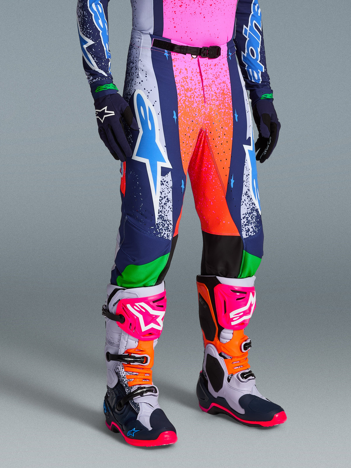 Alpinestars Limited Edition Supertech Records Pants, vibrant multicolor motocross pants with splattered pink and orange graphics, navy blue and white panels, featuring a large white and cyan Astars logo, worn with coordinating performance boots and gloves.