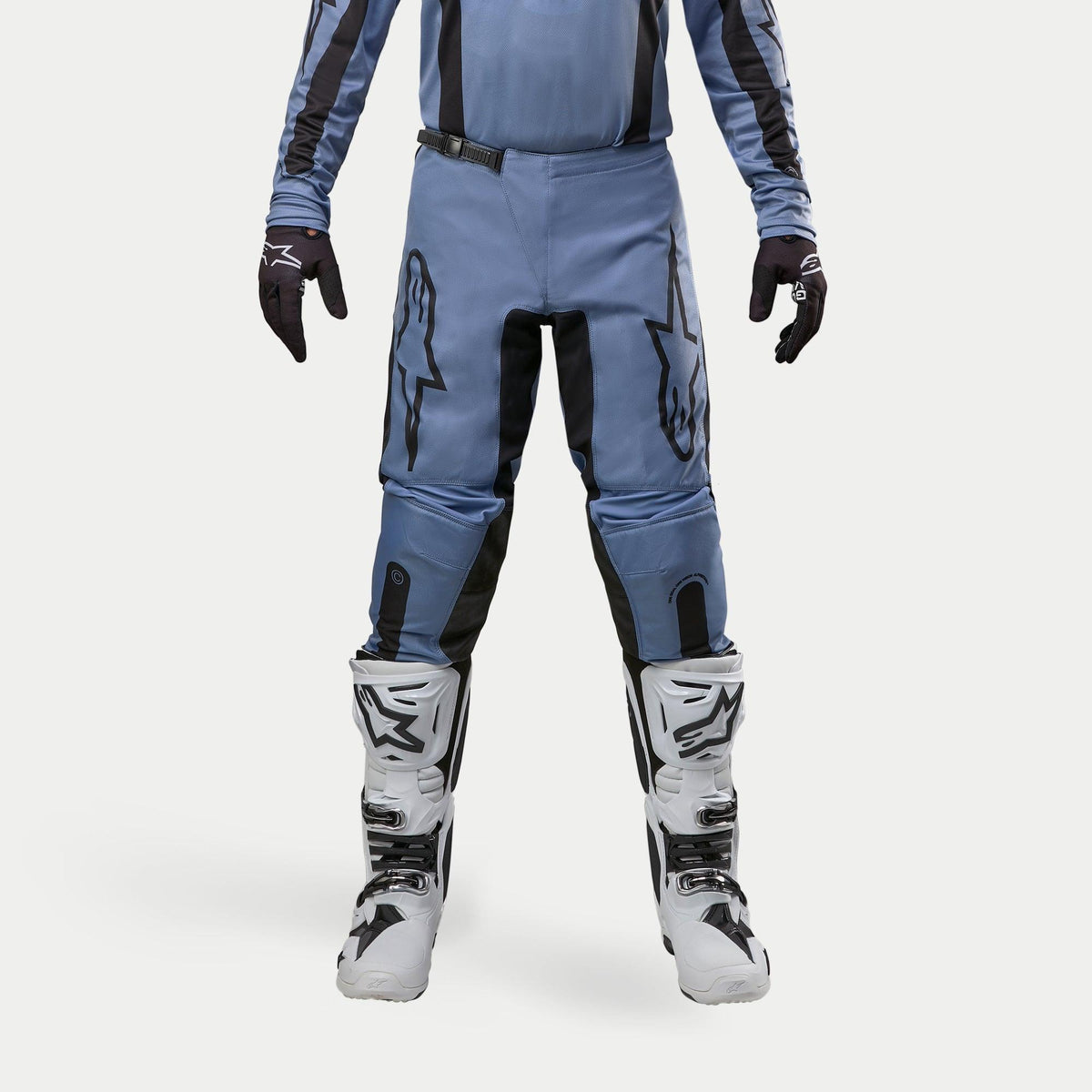 Alpinestars 2024 Fluid Lurv Hose, Motocross-Hose, Hellblau und Schwarz, getragen mit weißen und schwarzen Rennstiefeln und passenden Handschuhen, mit markanten schwarzen Stern-Logos auf den Oberschenkeln, ergonomisches Design für Offroad-Performance