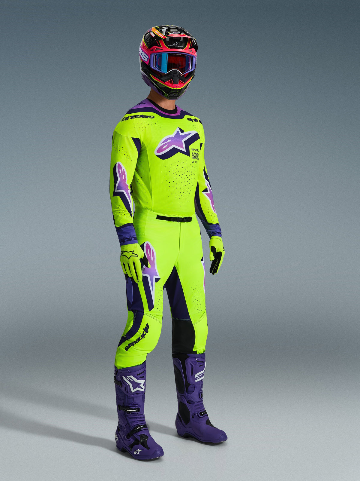 Alpinestars 2026 Supertech Vista Pants, Motocross Pants, Neon Yellow and Purple, worn with matching racing jersey, purple boots, and colorful helmet, featuring black leather knee panels, bold purple Astar logos, and perforated ventilation zones, coordinated outfit for off-road racing.