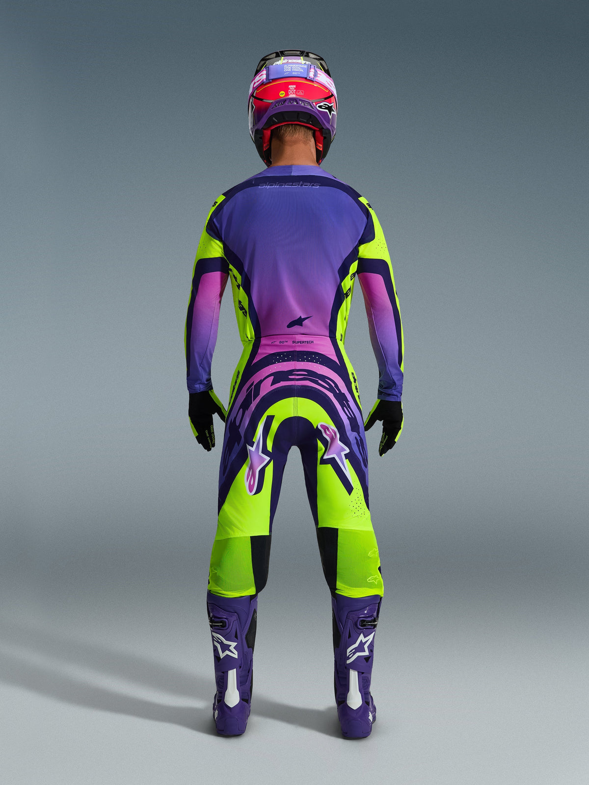 Alpinestars 2026 Supertech Vista Pants, Motocross Pants, Yellow Purple and Black, rear view of a motocross rider in a complete racing gear set with a purple gradient jersey and purple boots, vibrant athletic design for professional off-road racing