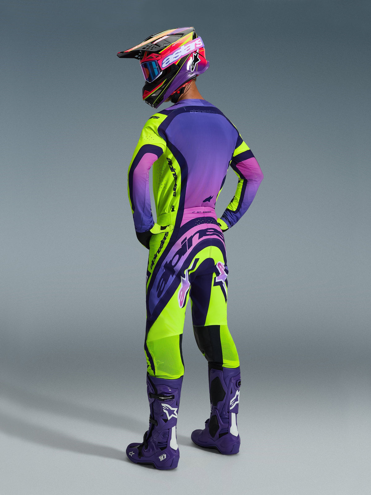 Alpinestars 2026 Supertech Vista Pants, Motocross Pants, Yellow Purple Black with pink gradients, back view of rider wearing matching jersey, purple racing boots, and multi-colored helmet, high-performance off-road gear.