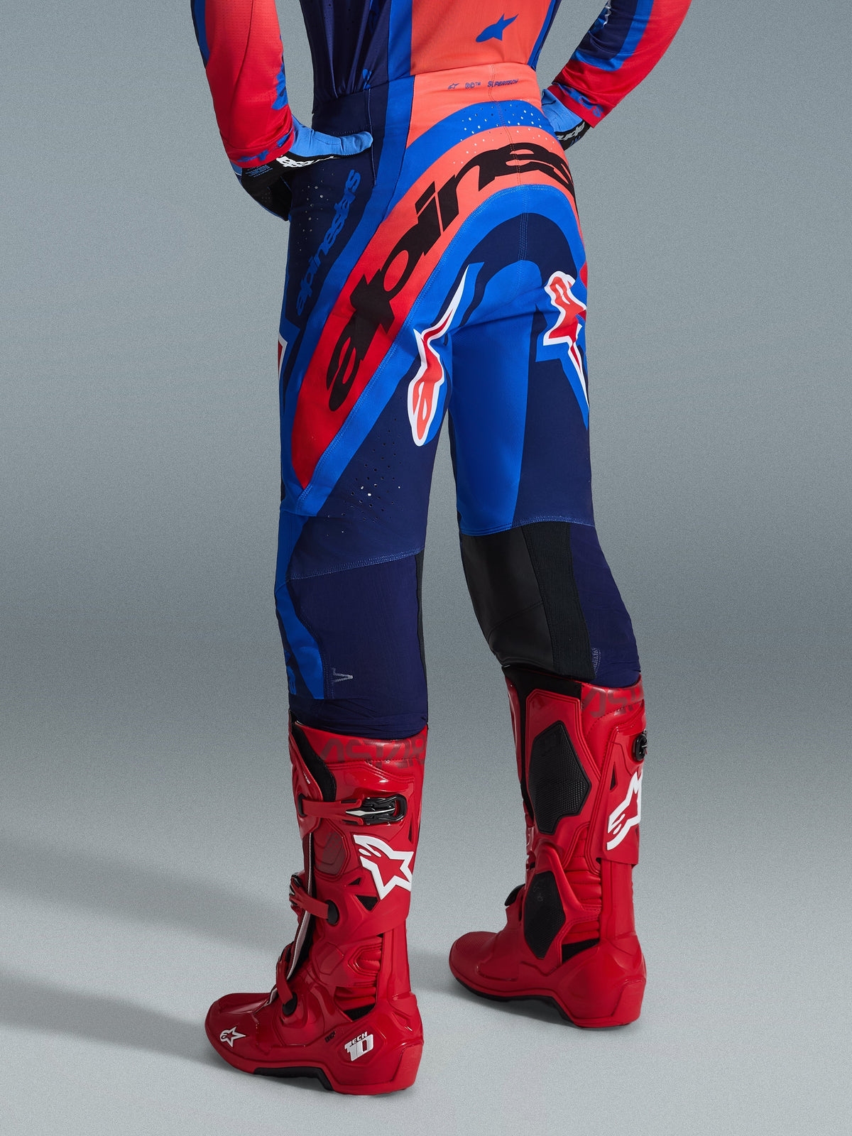 Alpinestars 2026 Supertech Vista Hose, Motocross-Hose, Dunkelblau, Hot Coral und Kobaltblau, Rückansicht des Fahrers, kombiniert mit roten Motocross-Stiefeln, markantes Branding am Gesäß, sportliche Passform mit Stretch-Zonen und robuster Rip-Stop-Konstruktion für den professionellen Rennsport
