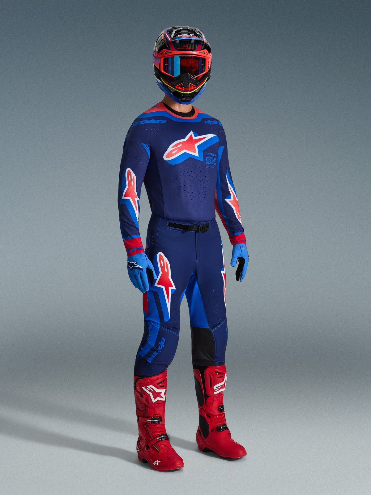 Motocross-Fahrer mit 2026 Supertech Vista Hose in Dark Navy Hot Coral Cobalt, passendem langärmeligem Renntrikot, roten Motocross-Stiefeln und abgestimmtem Helm mit roter Brille, Ganzkörper-Studioaufnahme einer leistungsstarken Offroad-Ausrüstung
