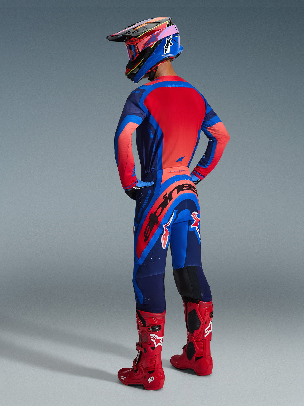 Alpinestars 2026 Supertech Vista Hose, Motocross-Hose, Dark Navy, Hot Coral und Cobalt, Rückansicht eines Fahrers in passendem Renntrikot und roten Stiefeln, markantes Branding am Gesäß und strapazierfähiges Stretchgewebe für Offroad-Performance.
