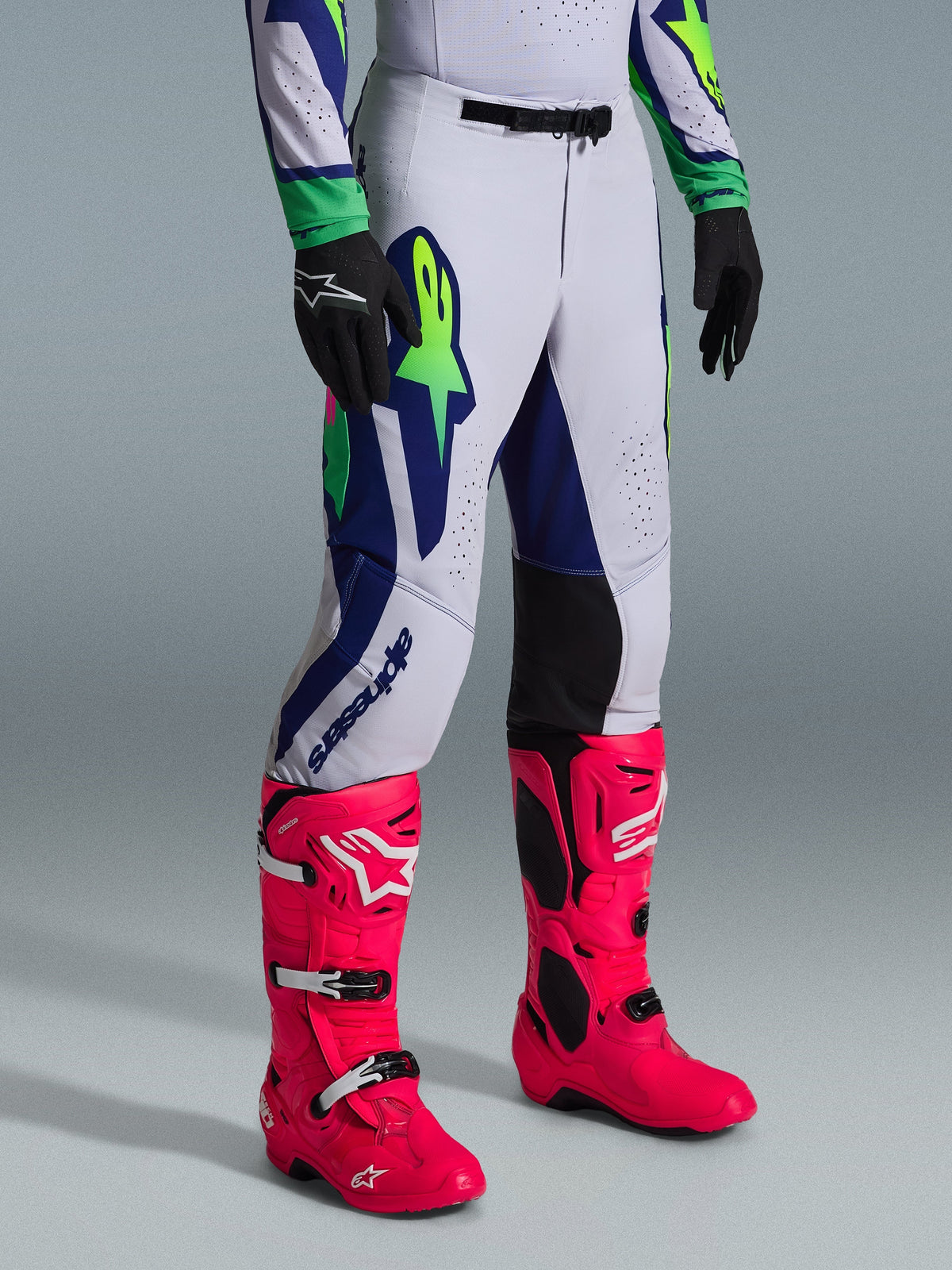 Alpinestars 2026 Supertech Vista Hose, Motocross-Hose, Hellgrau mit Gelb Fluo und blauen Akzenten, getragen mit leuchtend pinken Motocross-Stiefeln und schwarzen Handschuhen, athletische Rennpassform mit strapazierfähiger Stretch-Konstruktion für erstklassige Offroad-Performance