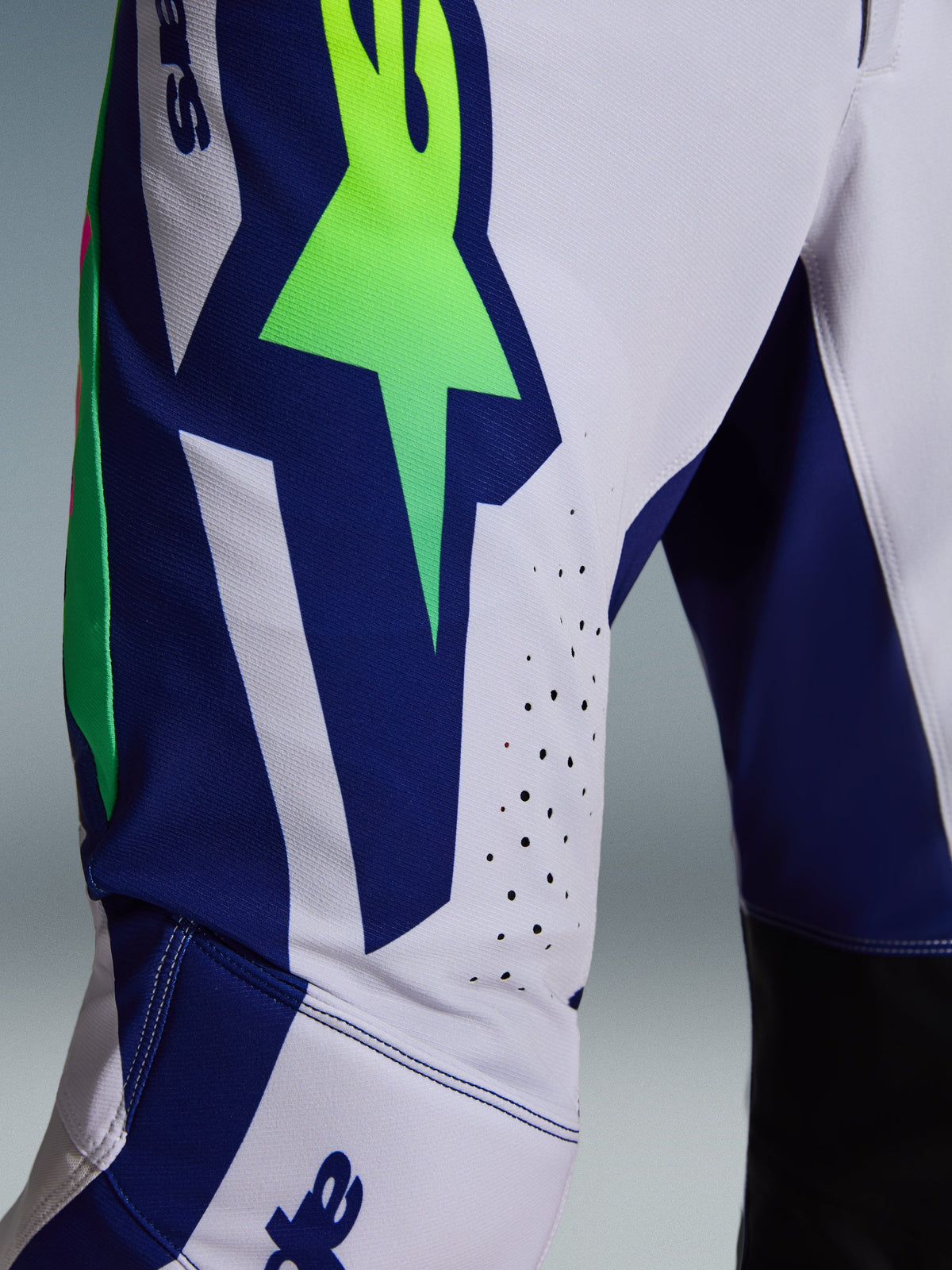 Alpinestars 2026 Supertech Vista Hose, Motocross-Hose, Hellgrau, Gelb Fluo und Blau, Nahaufnahme des Oberschenkel- und Kniebereichs mit einem markanten neongrünen Stern-Logo auf einem blauen Panel, lasergeschnittenen Perforationen zur Belüftung und schwarzen Knie-Innenpaneelen.
