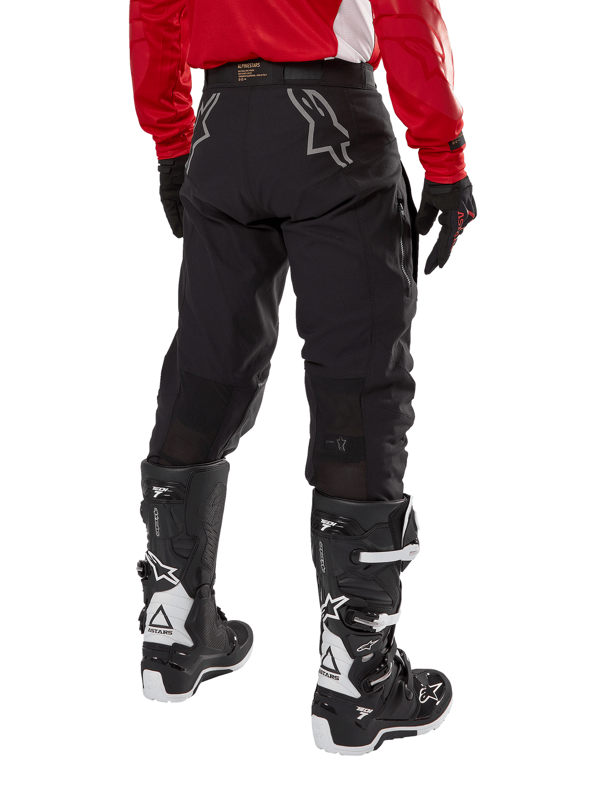 Alpinestars Techdura Hose, Offroad-Enduro-Hose, Schwarz, Rückansicht mit grauen Stern-Logos auf dem Gesäß, getragen mit einem roten langärmeligen Trikot und schwarz-weißen Tech 7 Stiefeln, robuste Textilkonstruktion für Abenteuerfahrten