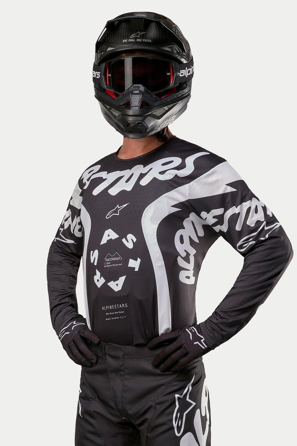 Alpinestars 2024 Racer Hana Jersey, Motocross-Jersey, Schwarz und Weiß, mit auffälligen weißen Alpinestars-Textgrafiken und Logo, getragen von einem Fahrer mit schwarzem Helm und Brille, Hochleistungs-Ausrüstung für den Offroad-Rennsport