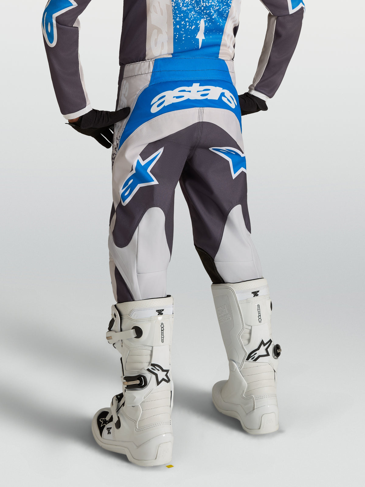 Alpinestars Fluid Drag Jugend-Hose 2027 in Grau und Blau, Motocross-Hose in der Rückansicht mit weißen Motorradstiefeln.