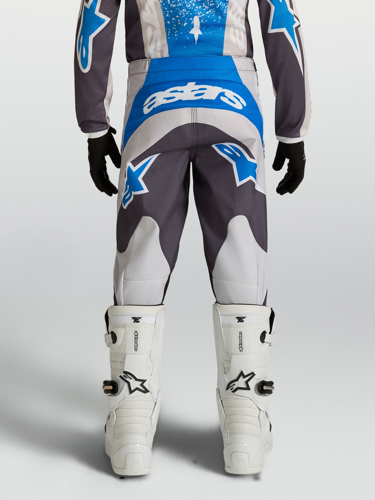 Alpinestars Fluid Drag Jugend-Hose 2027, Motocross-Hose für Kinder, Blau und Grau, Rückansicht mit weißen Tech 7 Stiefeln, strapazierfähiges 600D-Polygewebe.