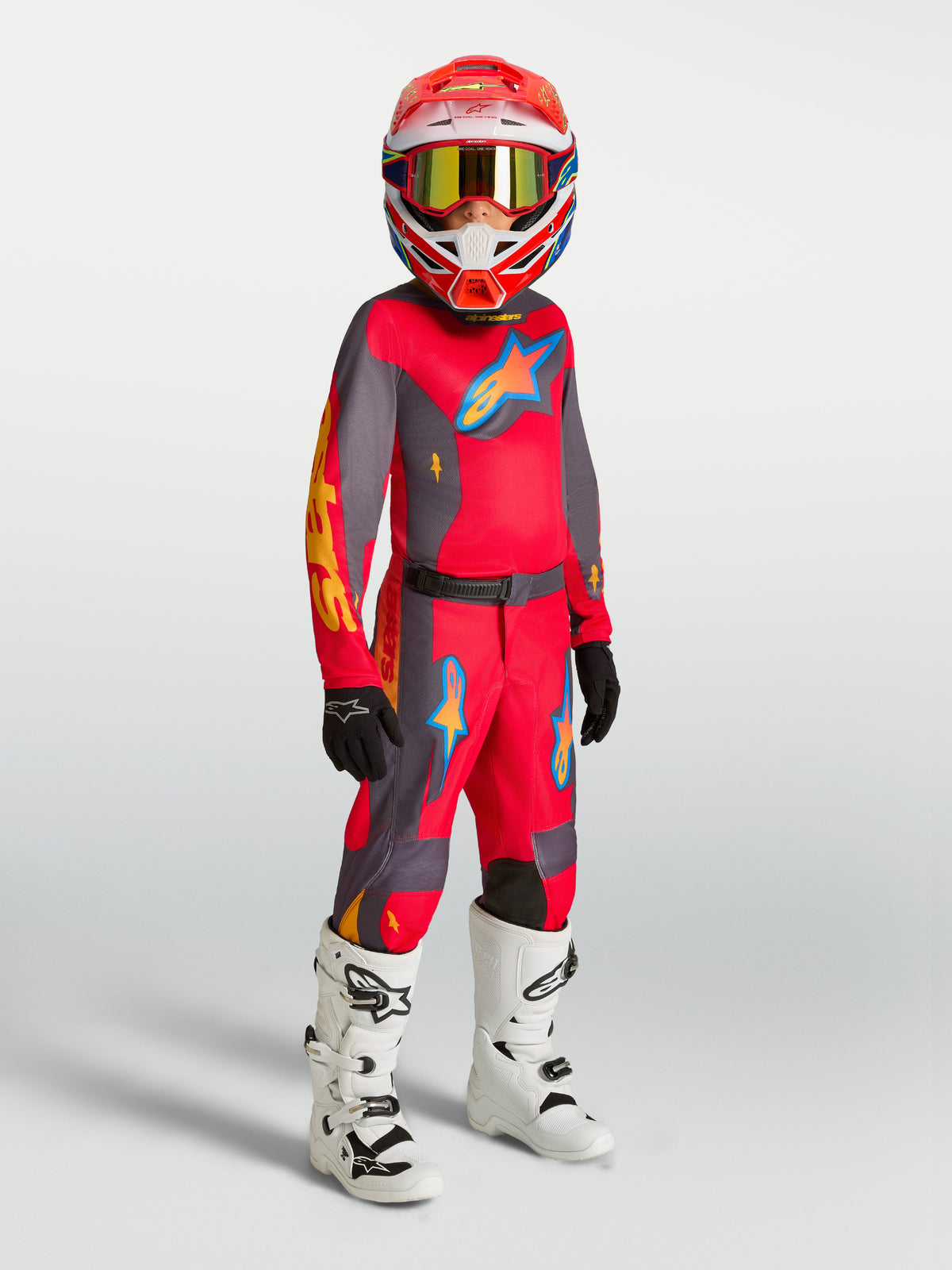 Alpinestars Jugend Fluid Hunt Hose, Motocross-Hose in Rot und Grau am Modell mit Trikot, weißen Stiefeln und Helm.