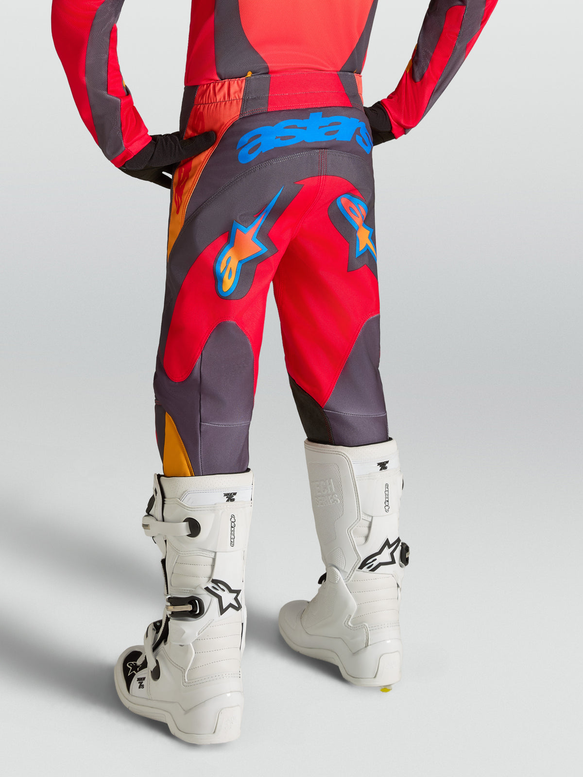 Alpinestars Jugend Fluid Hunt Hose 2027, Motocross-Hose, Rückansicht in Rot und Grau, strapazierfähiges 600D-Gewebe, Astars-Logo auf der Sitzfläche, getragen mit weißen Motocross-Stiefeln.
