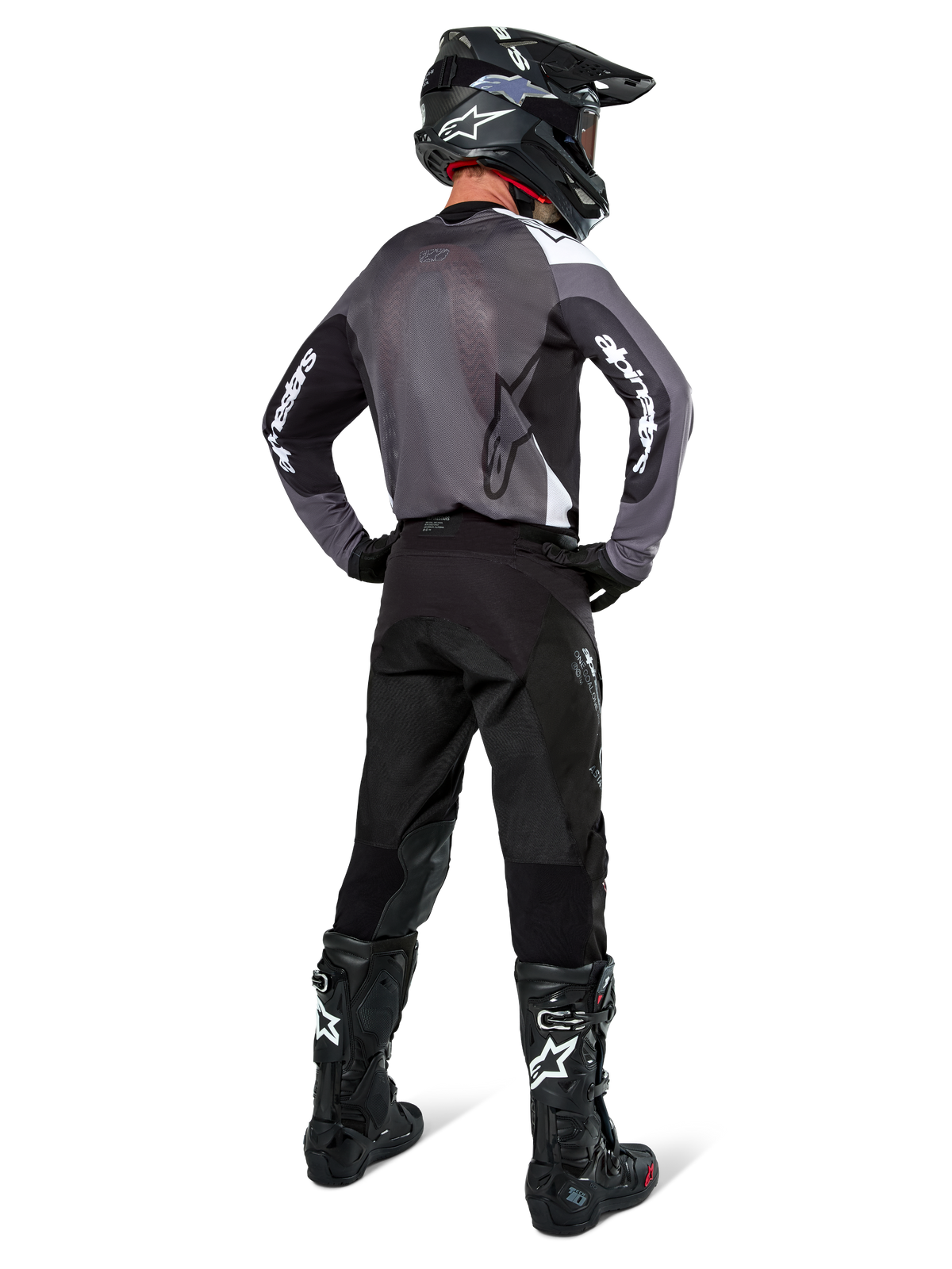 Motocross-Fahrer im Alpinestars Pro-Dura Trikot in Black Magnet White, Rückansicht mit grauem Mesh-Rückenteil und schwarzen Ärmeln mit weißem Alpinestars-Branding, kombiniert mit schwarzer Hose, schwarzem Helm und schwarz-weißen Stiefeln, professionelle Enduro-Rennausrüstung