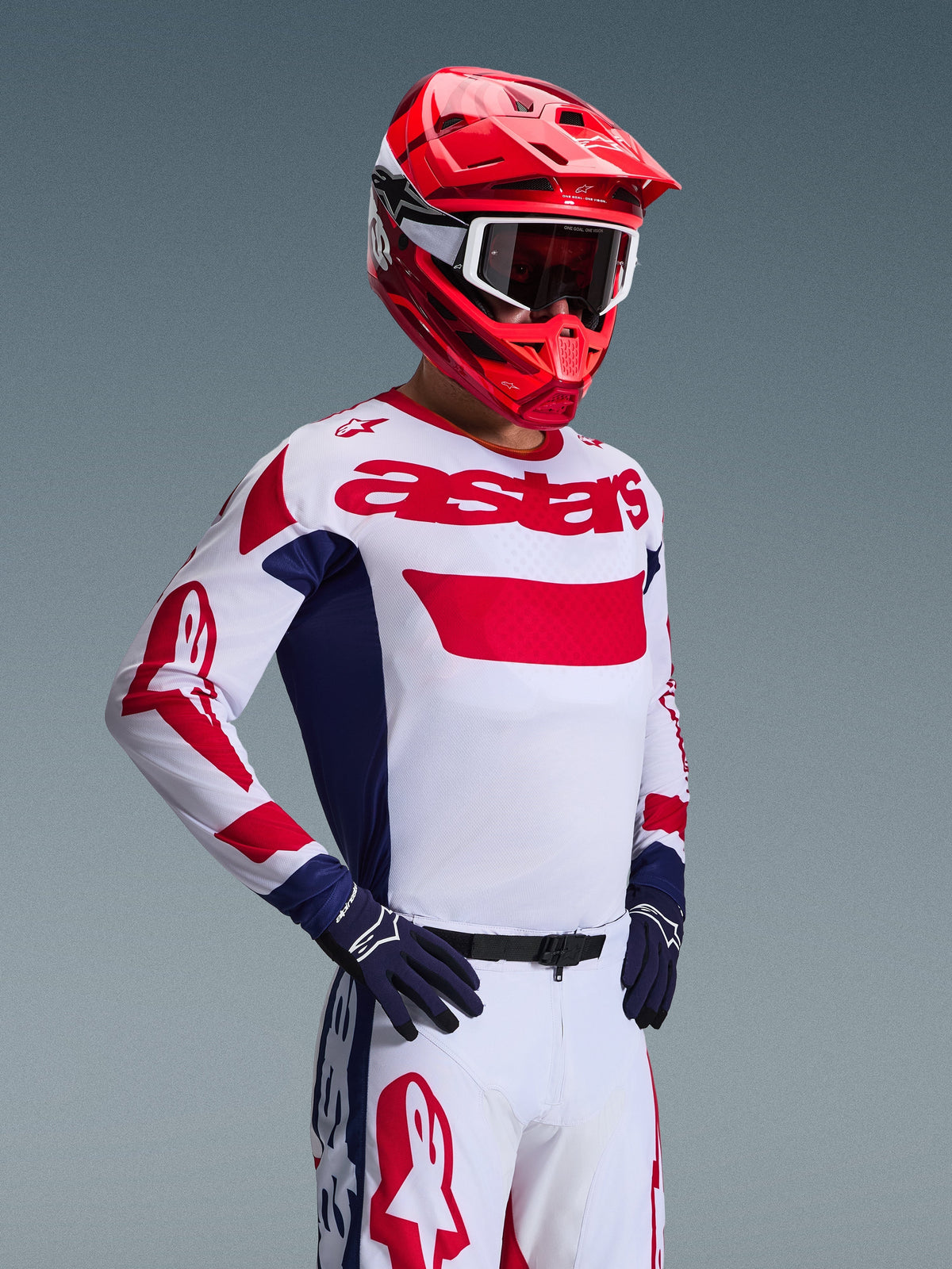 Motocross-Fahrer im Alpinestars 2026 Racer Riway Trikot in Weiß-Blau-Rot, passender Offroad-Hose, leuchtend rotem Helm mit weißer Schutzbrille und dunkelblauen Handschuhen, abgestimmte Hochleistungs-Ausrüstung für Motocross
