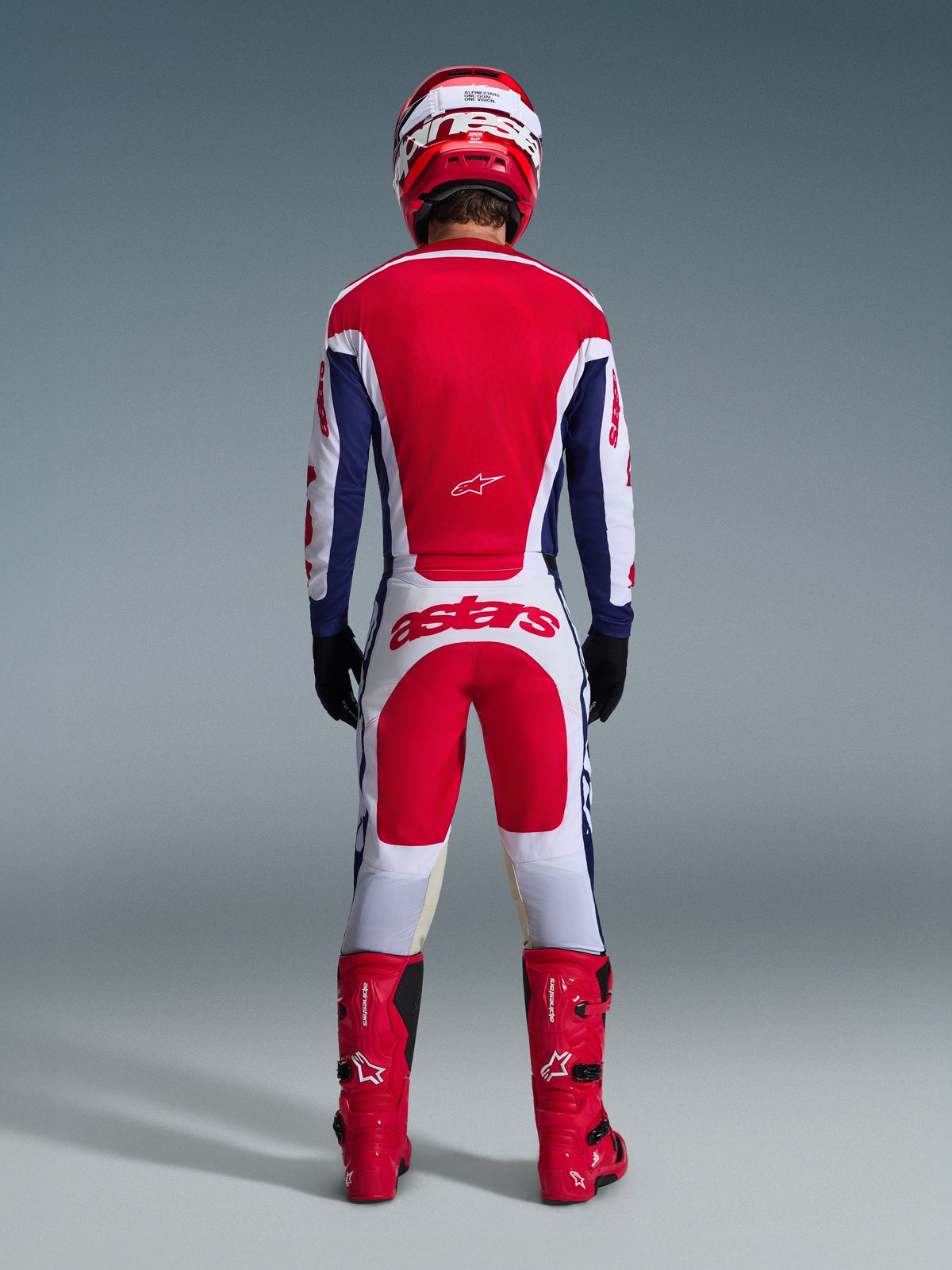 Motocross-Fahrer in der Rückansicht mit dem 2026 Racer Riway Ausrüstungsset, rot-blaues Trikot mit weißen Akzenten, weiße Hose mit roten Einsätzen und „astars“-Logo am Gesäß, kombiniert mit einem roten Helm, roten Stiefeln und schwarzen Handschuhen, Hochleistungs-Rennausrüstung für den Offroad-Einsatz