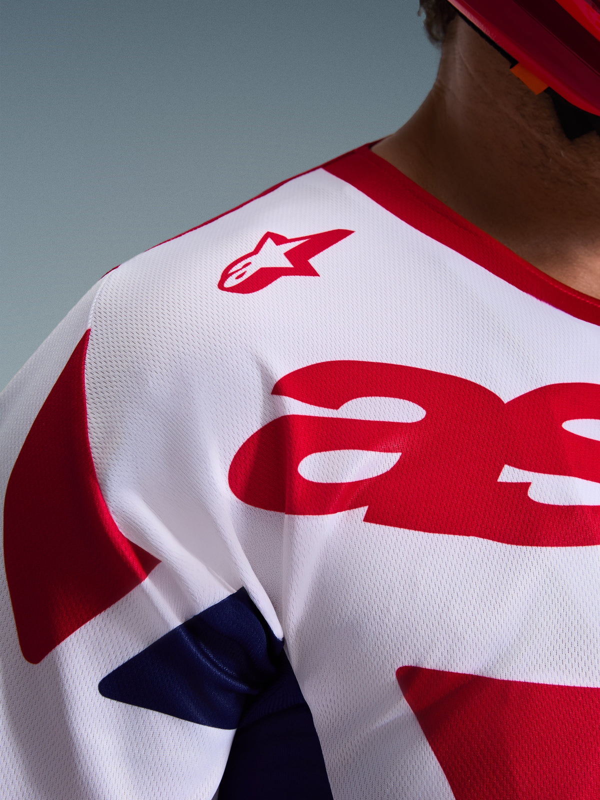 Nahaufnahme des Alpinestars 2026 Racer Riway Trikots in Weiß, Blau und Rot, die die atmungsaktive Mesh-Polygewebe-Konstruktion, das rote Alpinestars-Logo auf der Schulter und das feuchtigkeitsableitende Material für den Offroad-Rennsport hervorhebt.