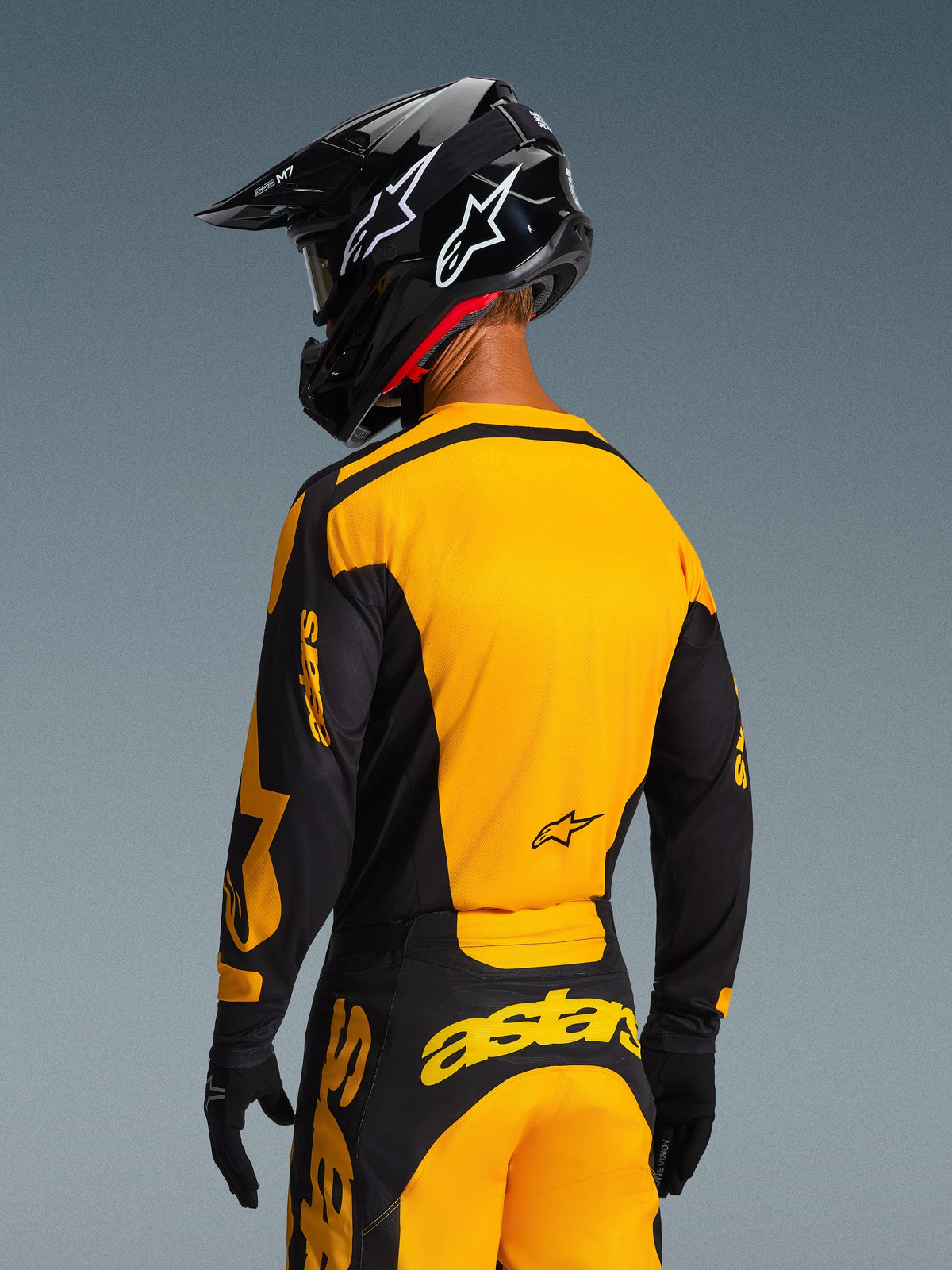 Rückansicht eines Motocross-Fahrers im Alpinestars 2026 Racer Riway Trikot in Gelb und Schwarz, mit auffälligem gelben Rückenpanel und schwarzen Ärmeln mit gelbem Branding, kombiniert mit einer passenden Motocross-Hose und einem schwarzen Helm für eine komplette Offroad-Rennausrüstung.