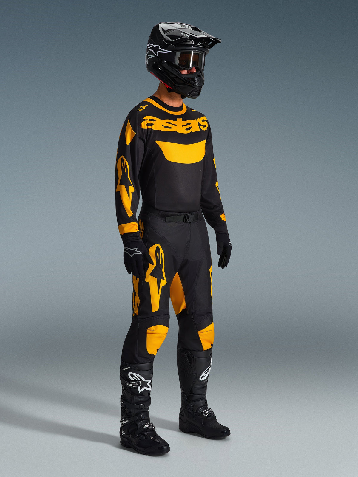 Motocross-Fahrer im 2026 Racer Riway Trikot in Gelb und Schwarz, komplette Rennausrüstung mit passender Hose, schwarzem Helm, Handschuhen und Stiefeln, entwickelt für Offroad-Performance mit auffälligen Alpinestars-Grafiken.