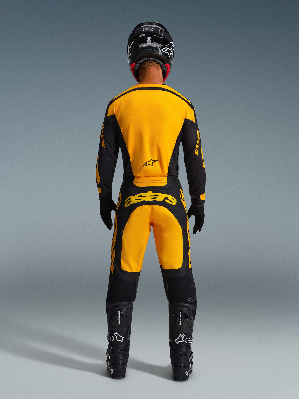 Motocross-Fahrer von hinten im 2026 Racer Riway Trikot und passender Hose in Gelb und Schwarz, schwarzer Helm, schwarze Stiefel und Handschuhe, komplette Offroad-Rennausrüstung mit markantem Alpinestars-Branding.