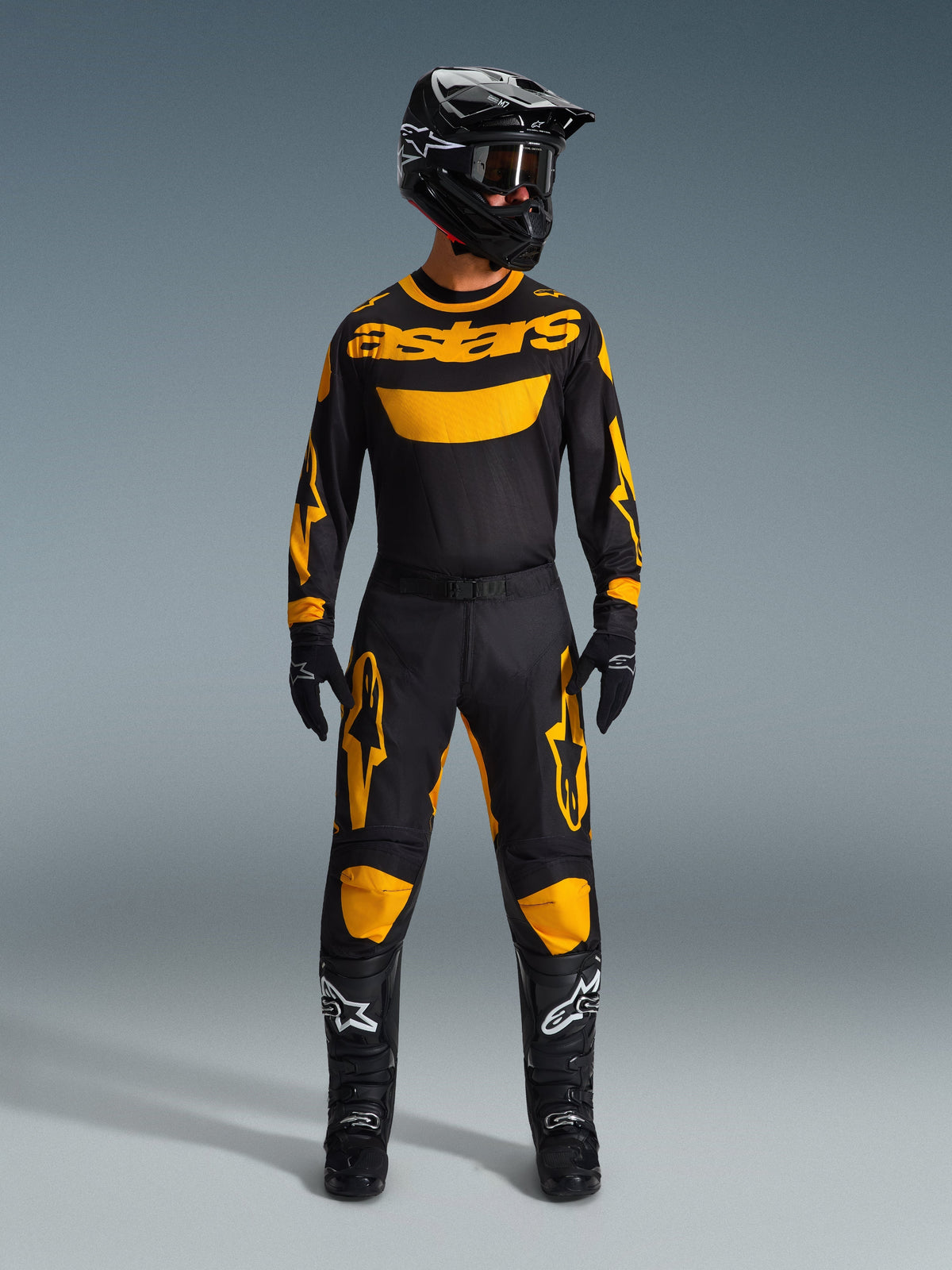 Motocross-Fahrer im 2026 Racer Riway Trikot in Gelb und Schwarz, kombiniert mit passender Hose, schwarzem Helm und schwarzen Stiefeln mit weißen Alpinestars-Logos, komplette Ausrüstung für den Offroad-Rennsport