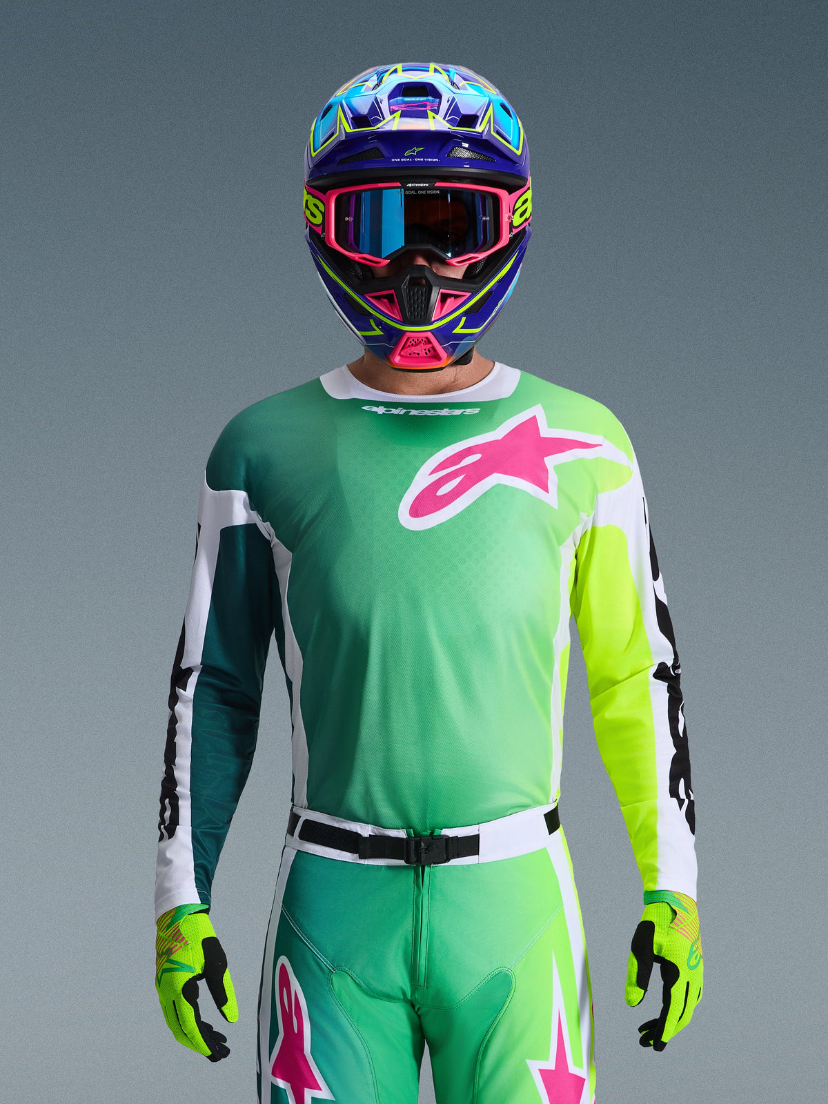 Alpinestars 2026 Racer Portl Gear Set, Motocross-Fahrer trägt Trikot mit grünem und gelbem Farbverlauf sowie pinkfarbenem Astars-Logo, passende Hose, bunter blau-pinker Helm mit blauer Brille und lindgrüne Handschuhe, abgestimmtes professionelles Offroad-Rennoutfit