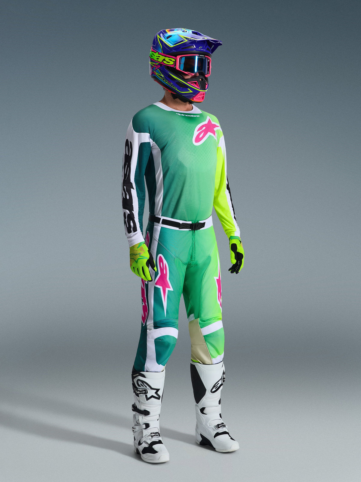 Motocross-Fahrer in kompletter Rennausrüstung, 2026 Racer Portl Trikot in Grün mit weiß-schwarzen Ärmeln und pinkfarbenem Logo, passende grüne Hose mit pinkfarbenen Akzenten, mehrfarbiger Helm mit Brille, weiß-schwarze Stiefel und grüne Handschuhe, abgestimmtes Outfit für den Offroad-Rennsport